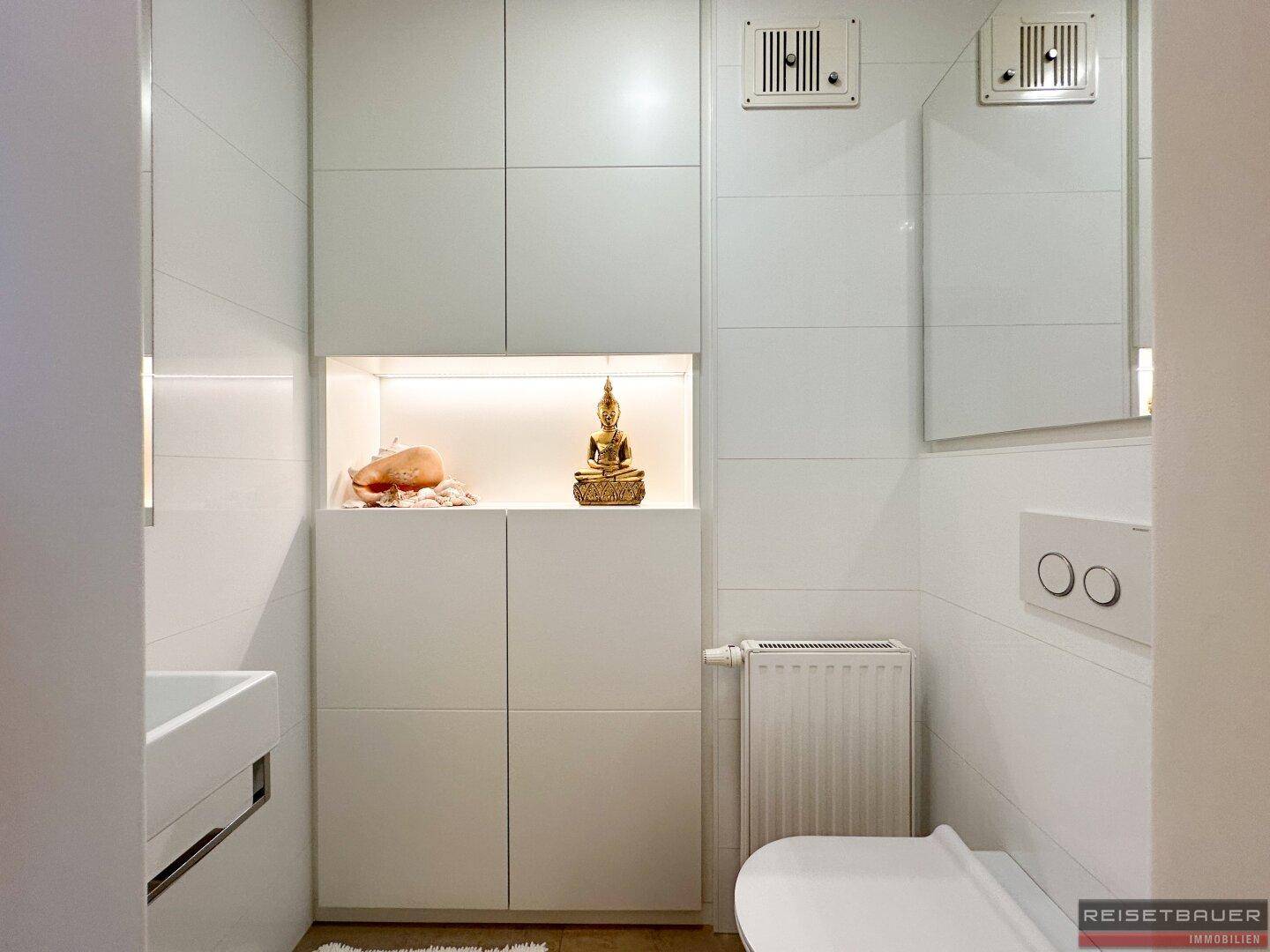 Kleines, modernes WC mit weißen Fliesen, wandmontierter Toilette und integrierten Schränken.