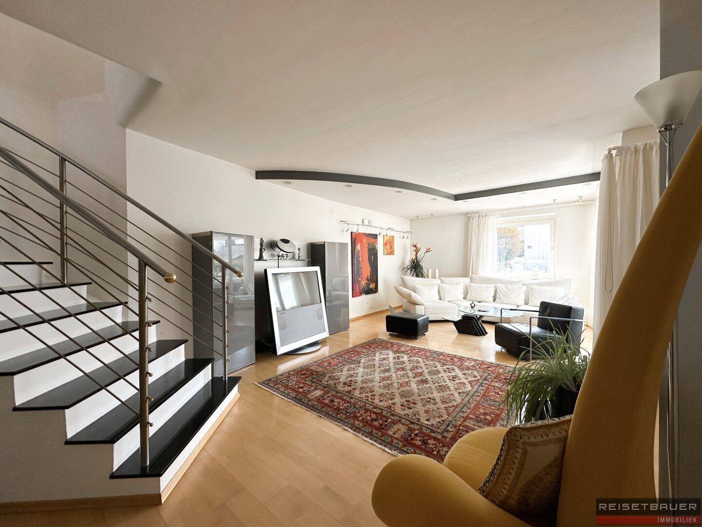Geräumiges Wohnzimmer mit Holzboden, großem Teppich und einer modernen Treppe, die in die obere Etage führt.