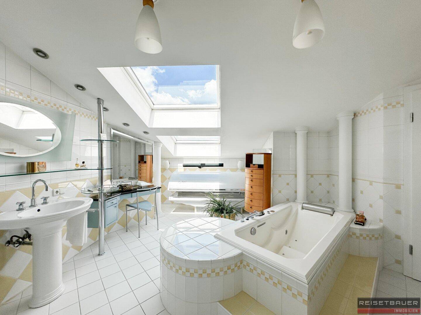 Helles Badezimmer mit Badewanne, Dusche, zwei Waschbecken und einem großen Dachfenster.