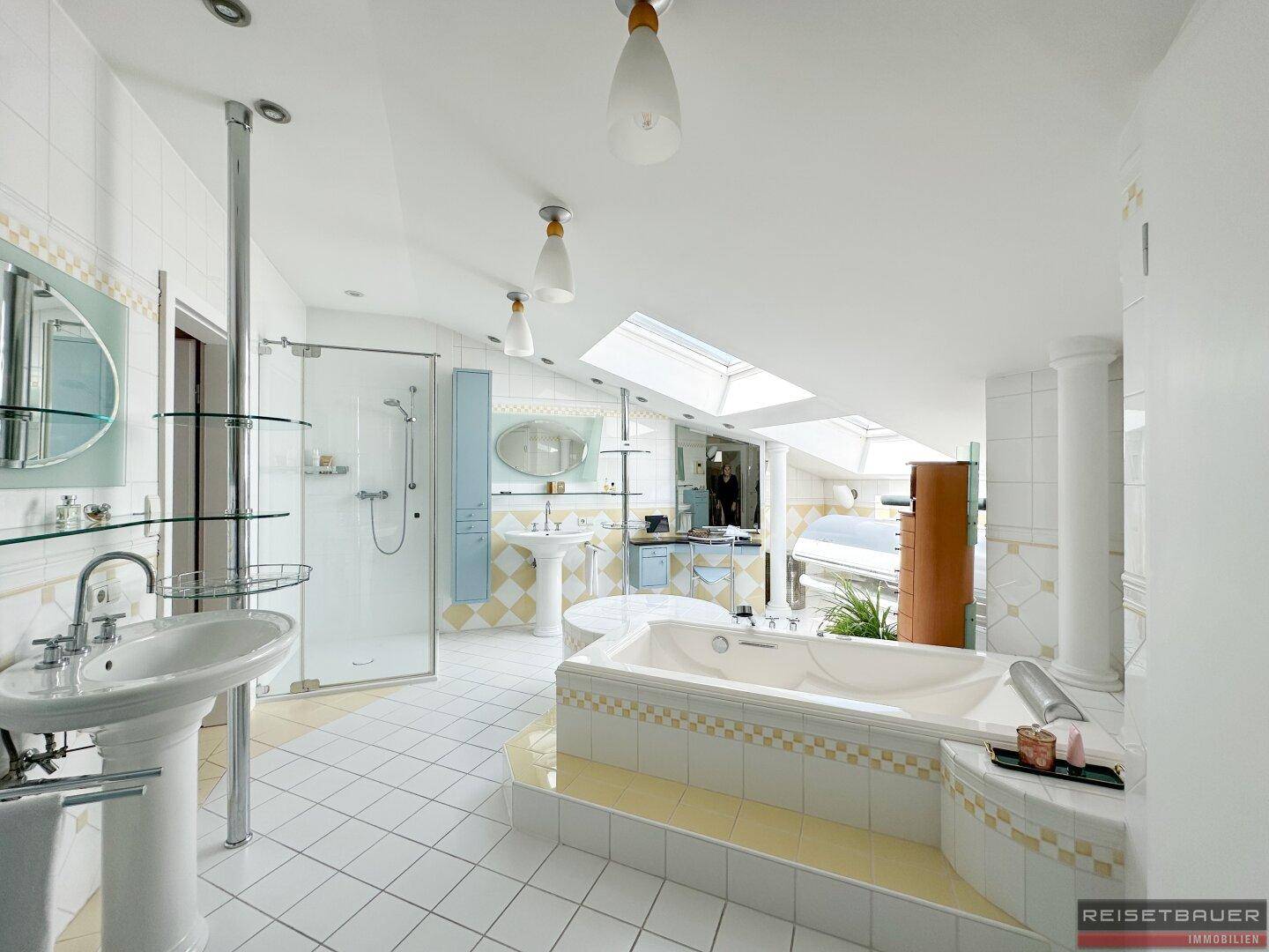 Großes Badezimmer mit Badewanne, Dusche, zwei Waschbecken und viel Tageslicht durch Dachfenster.
