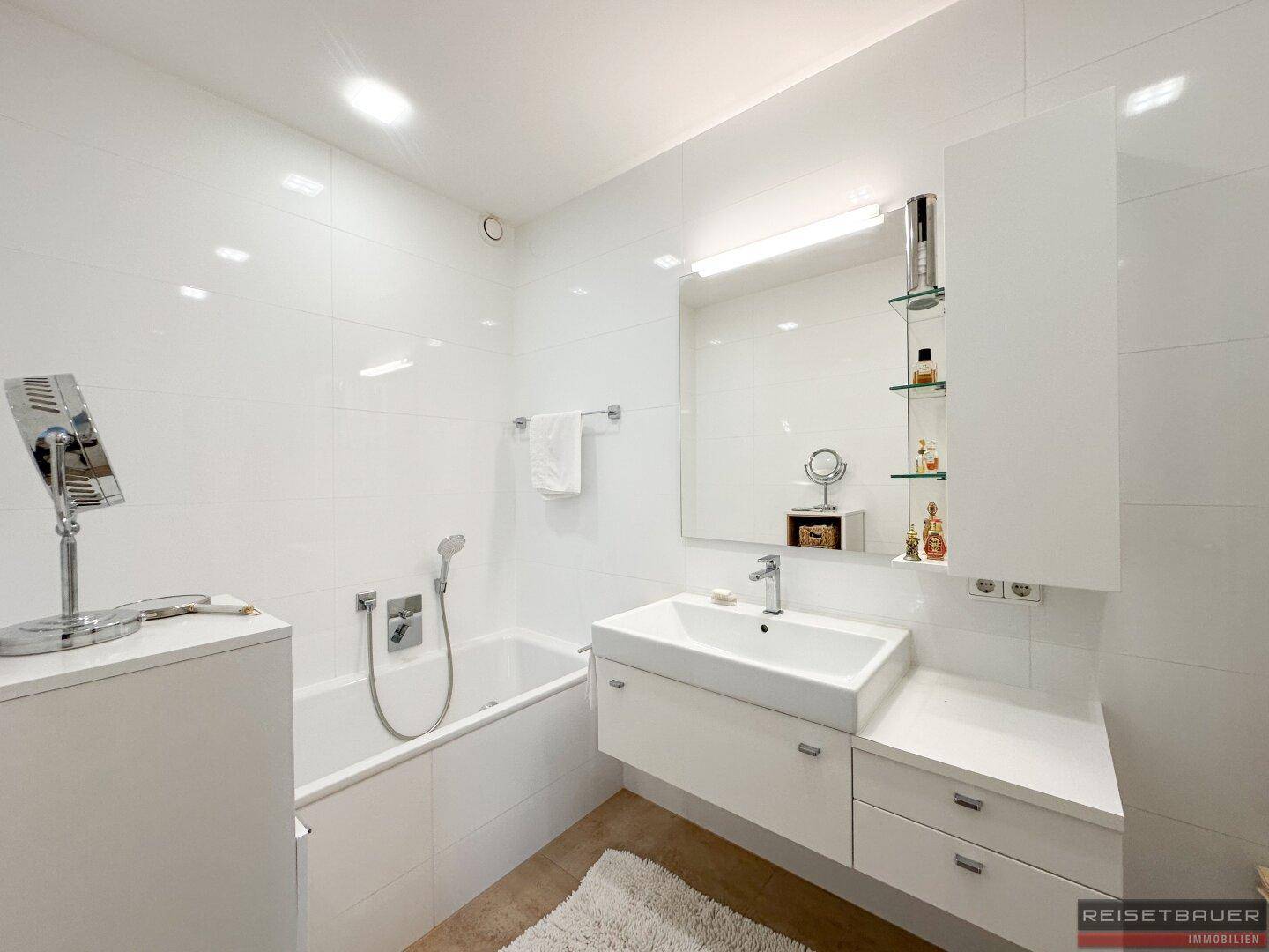 Modernes Badezimmer mit weißen Fliesen, Badewanne und einem eleganten Waschtisch mit Unterschrank.