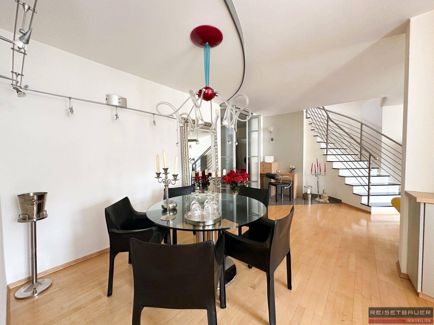 Eleganter Essbereich mit Holzboden, modernem Glastisch und einem großen Spiegel, der den Raum erweitert.