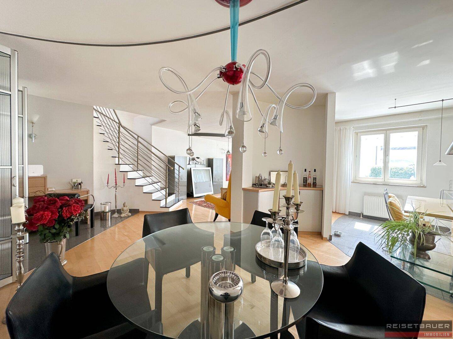 Stilvoller Essbereich mit rundem Glastisch, schwarzen Stühlen und einer auffälligen Designerlampe.