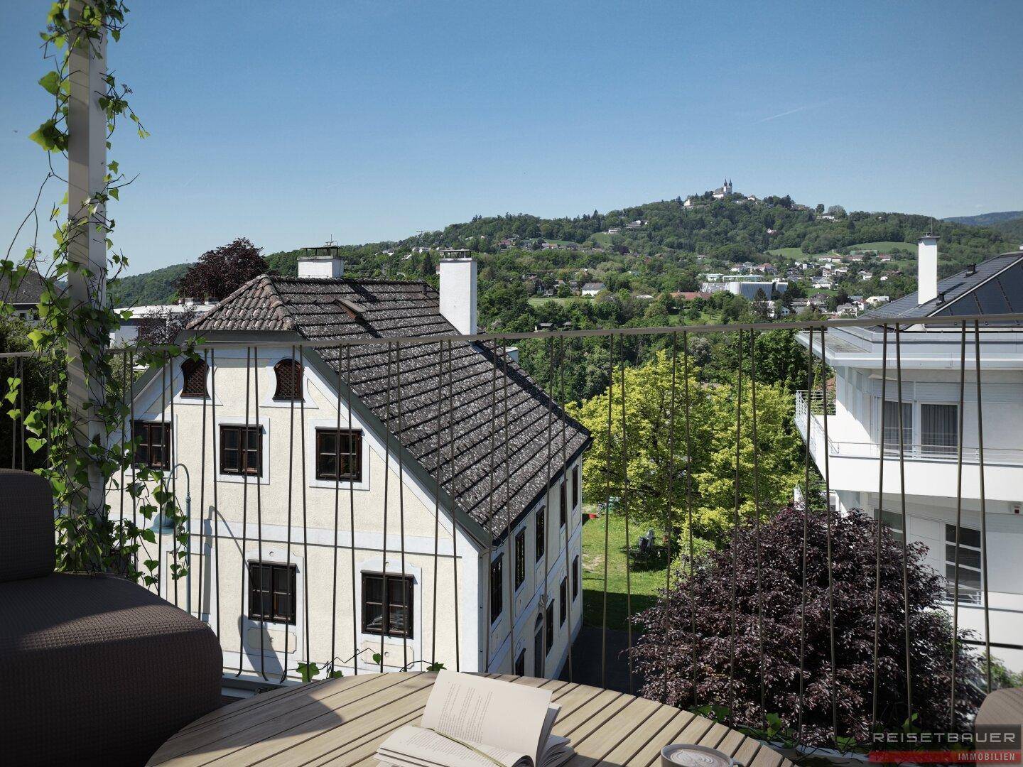 Blick vom Balkon auf ein traditionelles Gebäude und grüne Hügel mit einer Burg in der Ferne.
