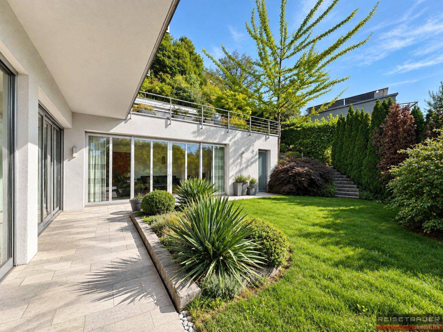 Gepflegter Gartenbereich mit Terrasse, üppiger Bepflanzung und Treppenaufgang.