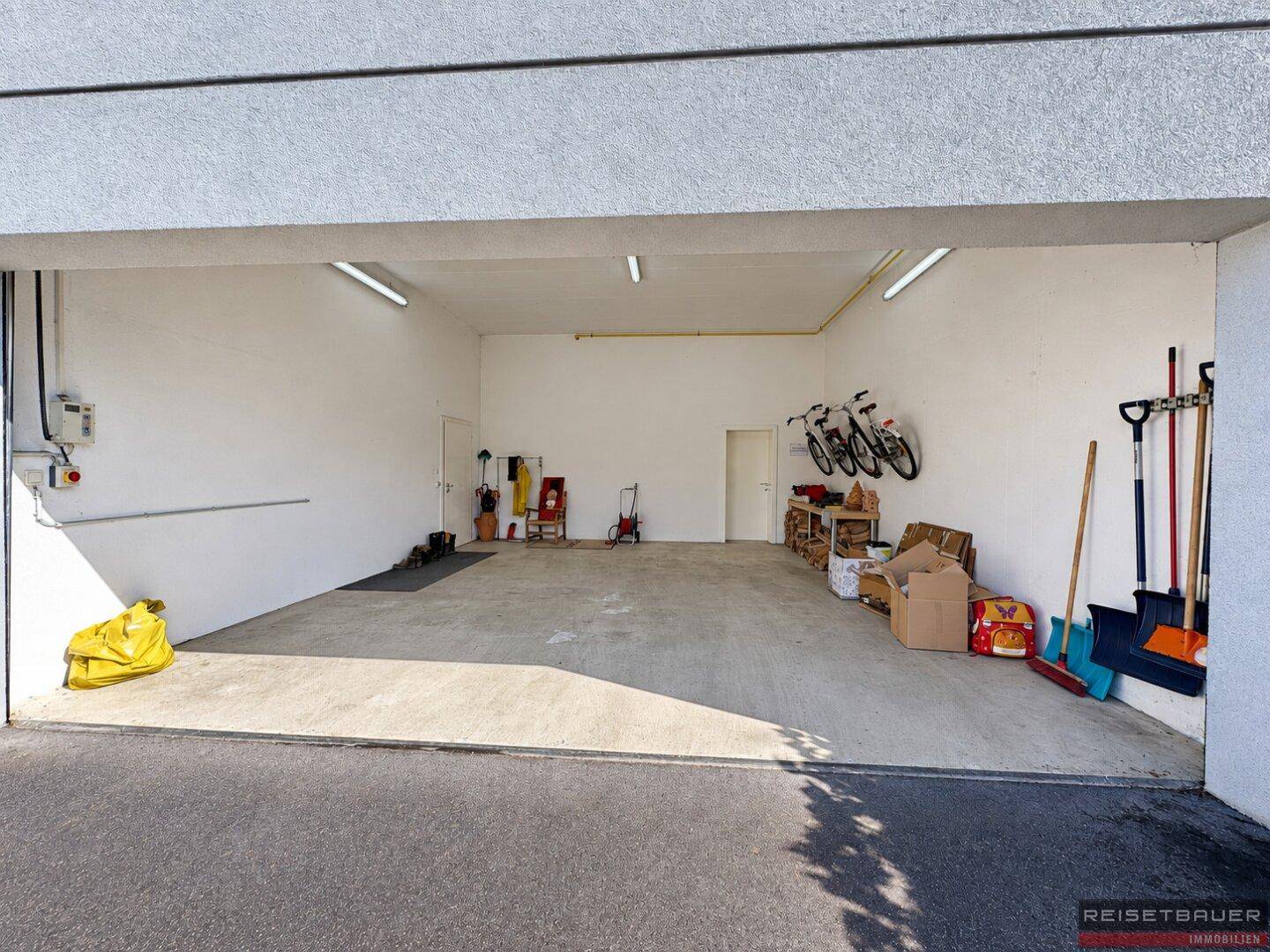 Geräumige Garage mit viel Stauraum für Fahrräder und Gartengeräte, hell beleuchtet.