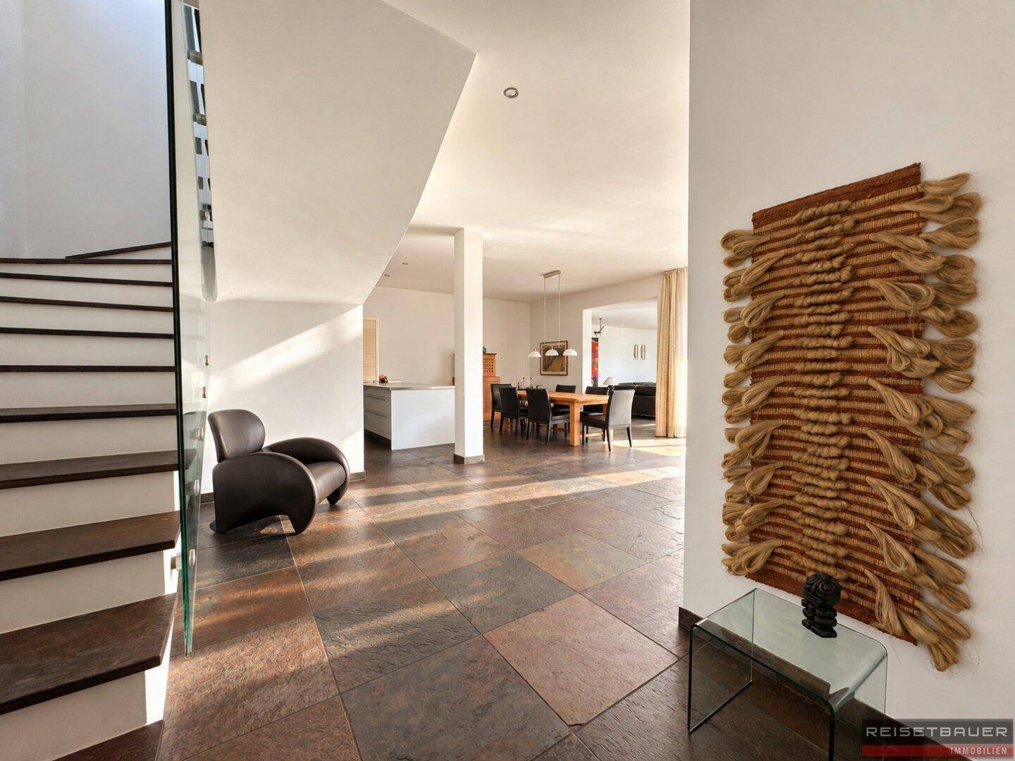 Heller Eingangsbereich mit Natursteinfliesen, moderner Treppe und dekorativer Wandkunst.
