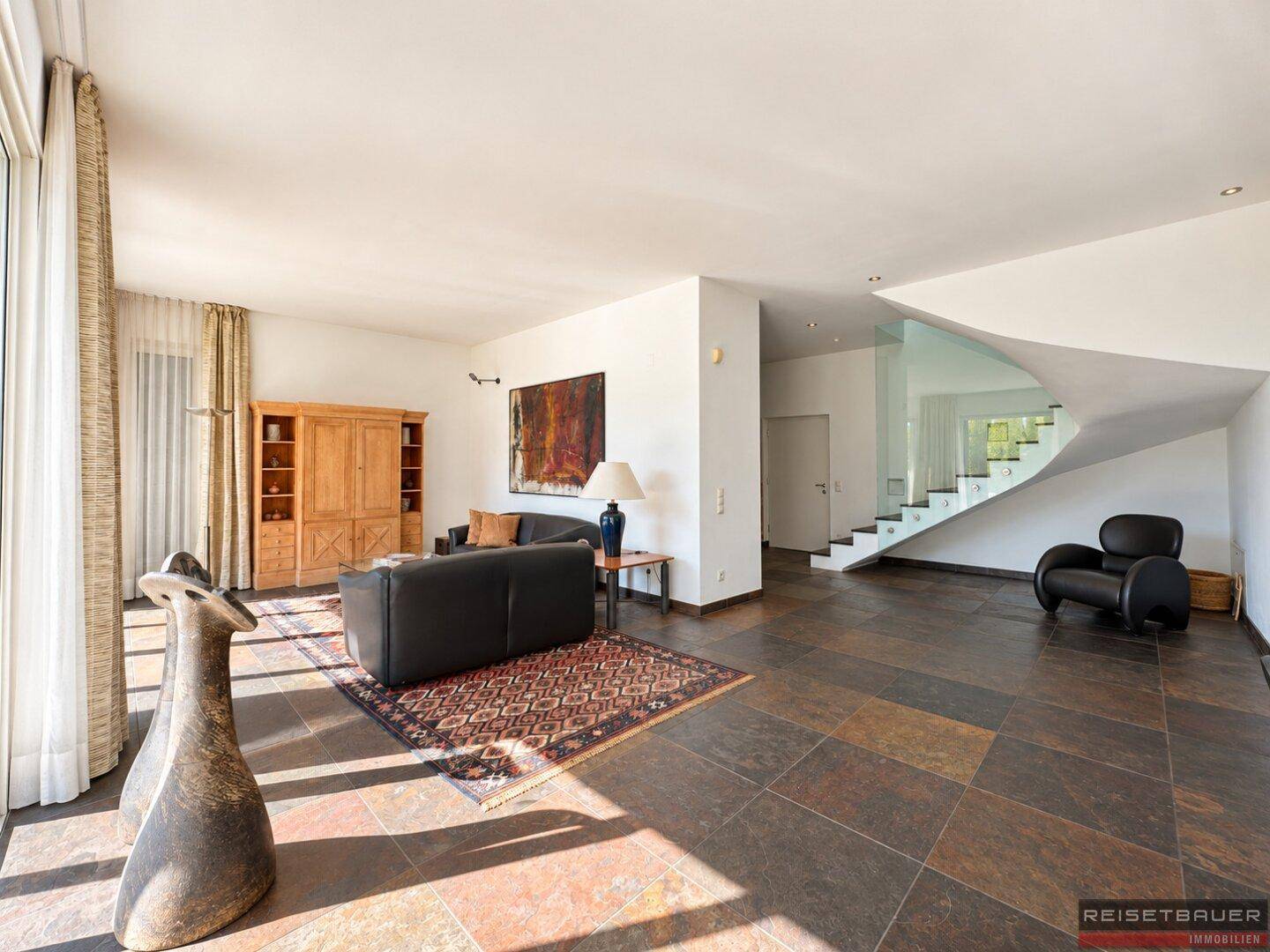 Geräumiges Wohnzimmer mit dunklen Fliesen, bequemen Sofas und einer eleganten Wendeltreppe.