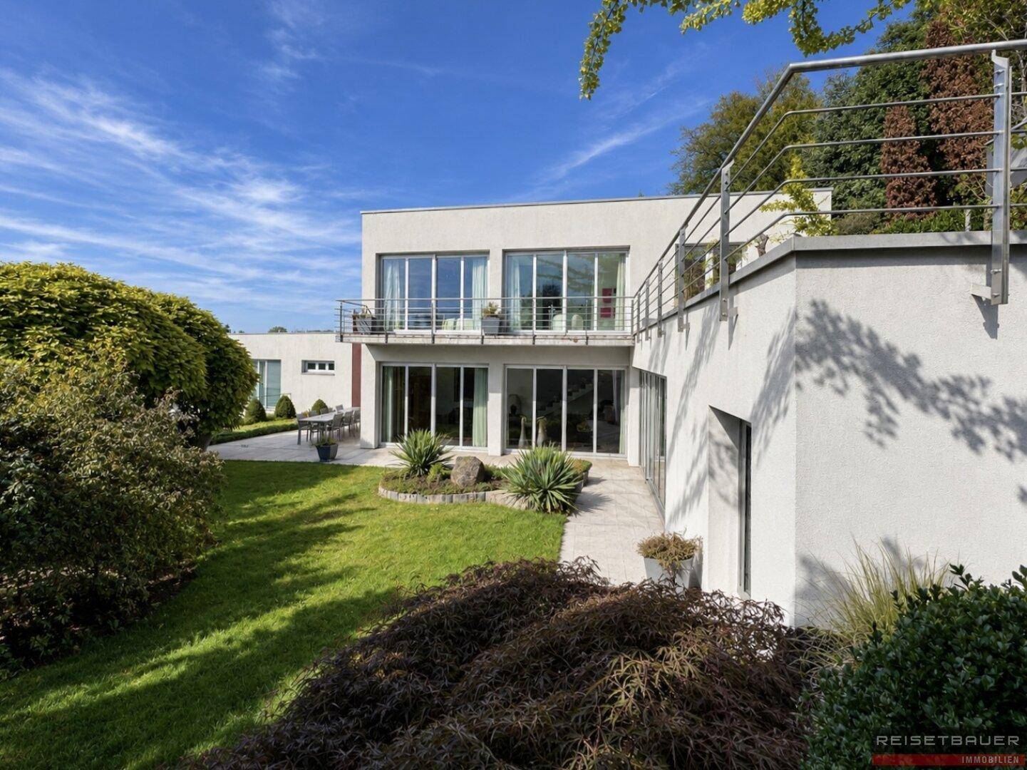 Moderne Villa mit weitläufigem Garten, gepflegter Rasenfläche und sonnigen Terrassen.