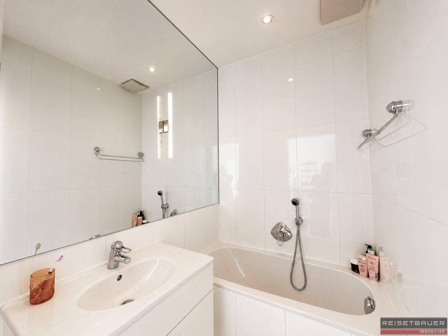 Helles Badezimmer mit Badewanne, Einzelwaschbecken und großen Wandspiegeln.