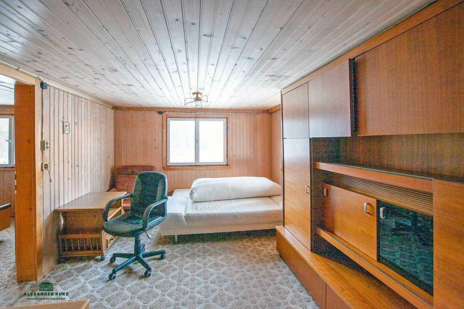 Einfaches Schlafzimmer mit Holztäfelung, Einzelbett, Schreibtisch und Teppichboden.