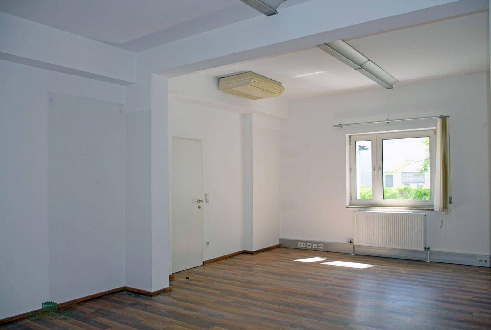 Heller Raum mit Laminatboden, weiß gestrichenen Wänden und einem Fenster, das Tageslicht hereinlässt.