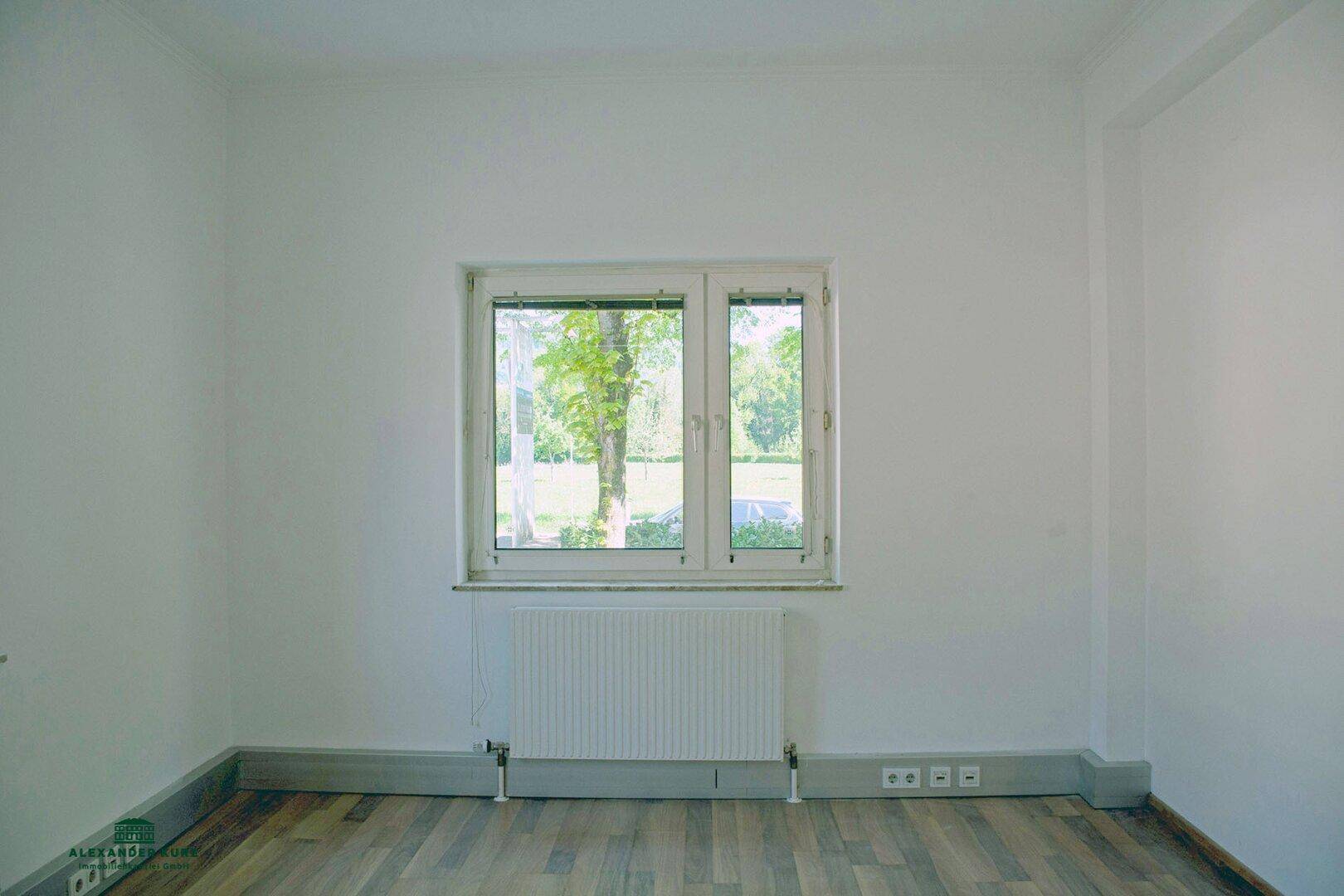 Leerer Raum mit Holzboden und einem Fenster, das einen schönen Blick ins Grüne bietet.