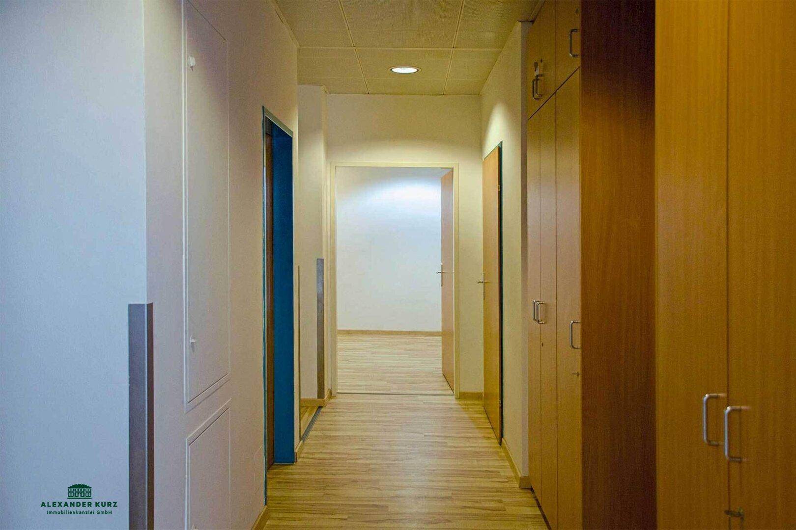 Langer Flur mit Laminatboden, weißen Wänden und integrierten Holzschränken, der zu weiteren Räumen führt.