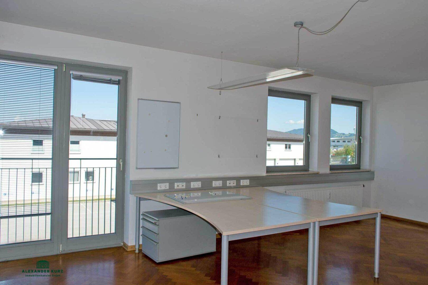 Büro mit Parkettboden, großen Fenstern und einem Schreibtisch, der viel Arbeitsfläche bietet.