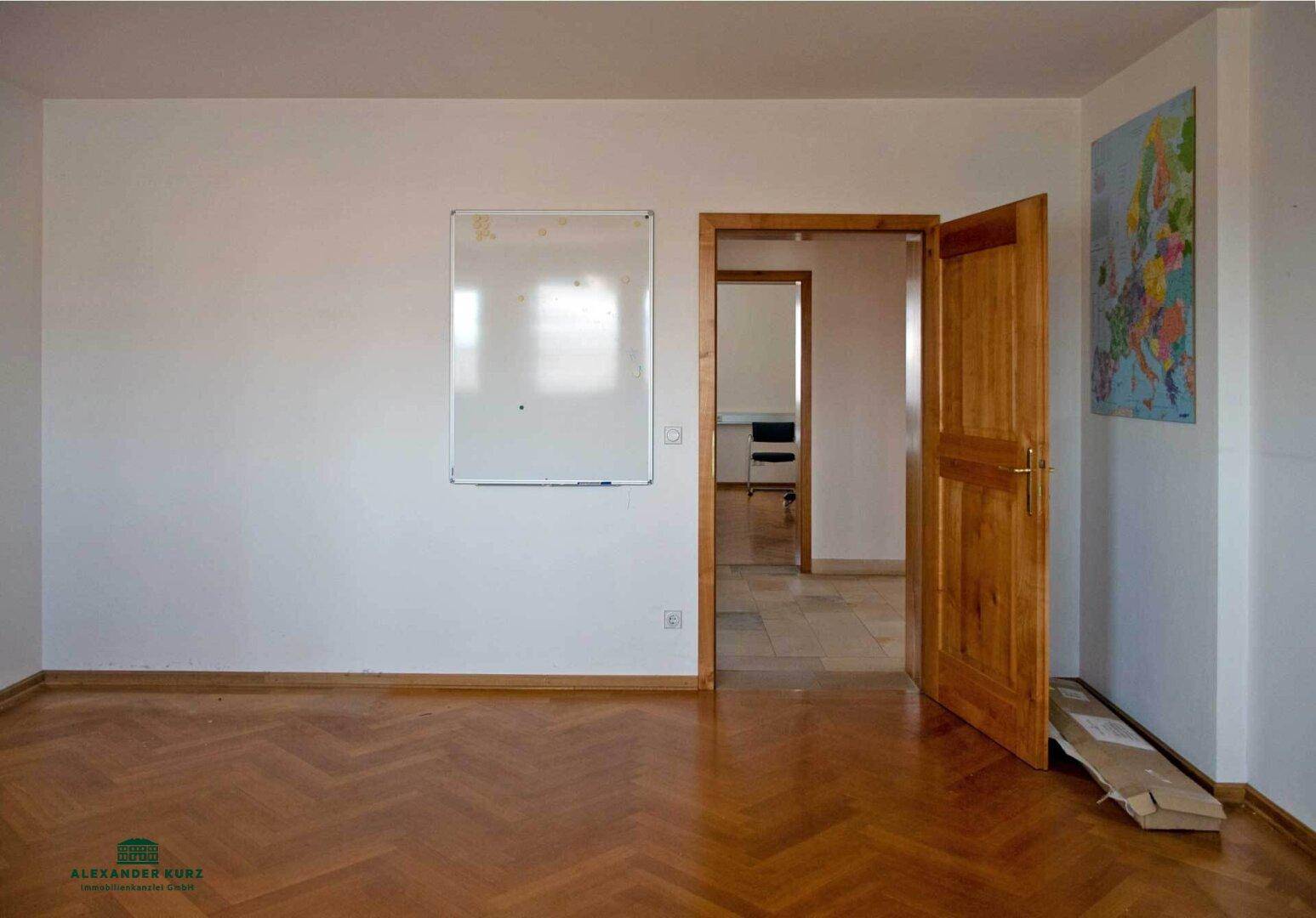 Leeres Büro mit Fischgrätparkett, einer Holztür und einer weißen Wandtafel, bereit zur Einrichtung.