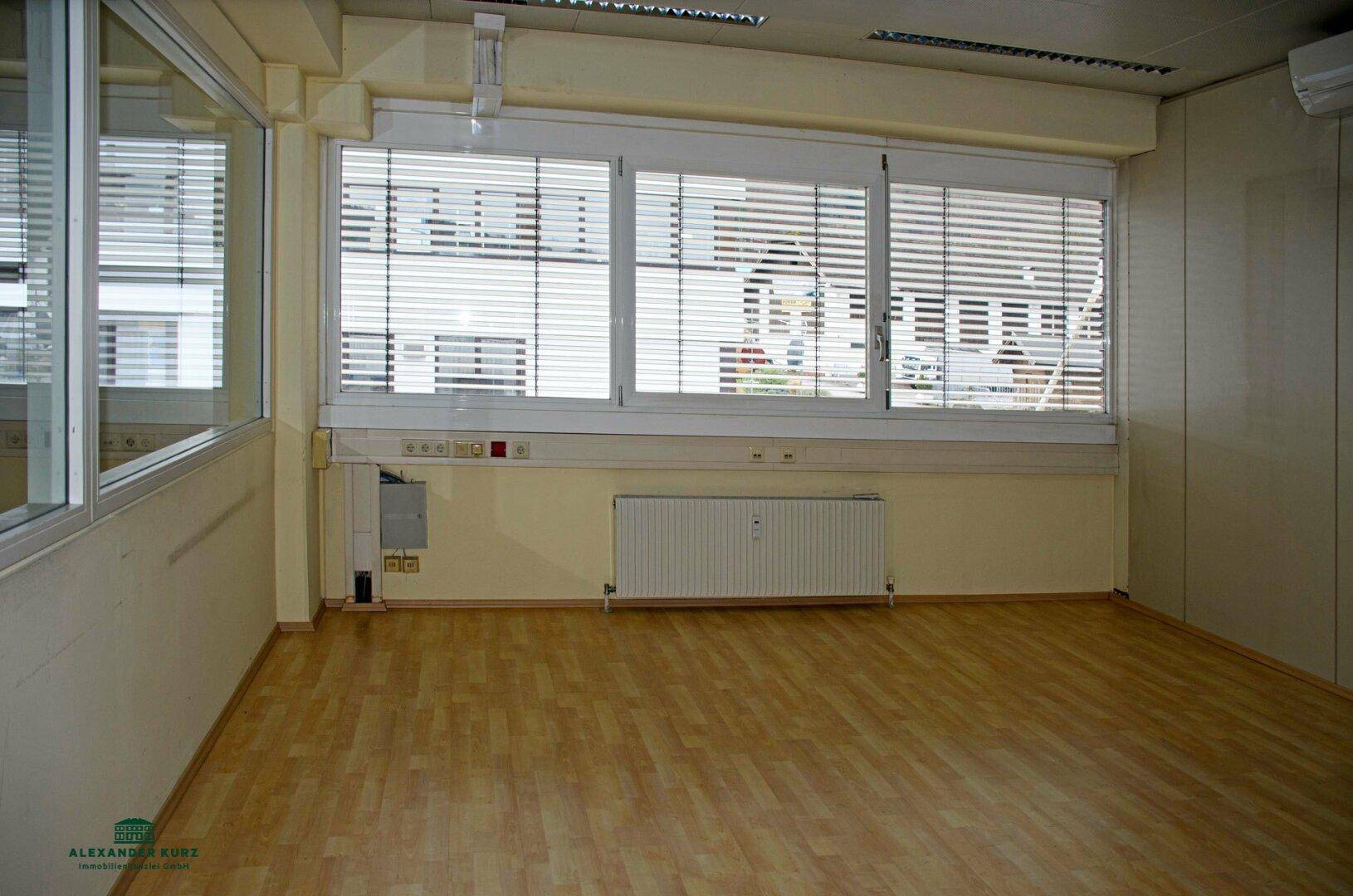 Helles und geräumiges Büro mit großen Fenstern, Jalousien, Heizkörper und Laminatboden.