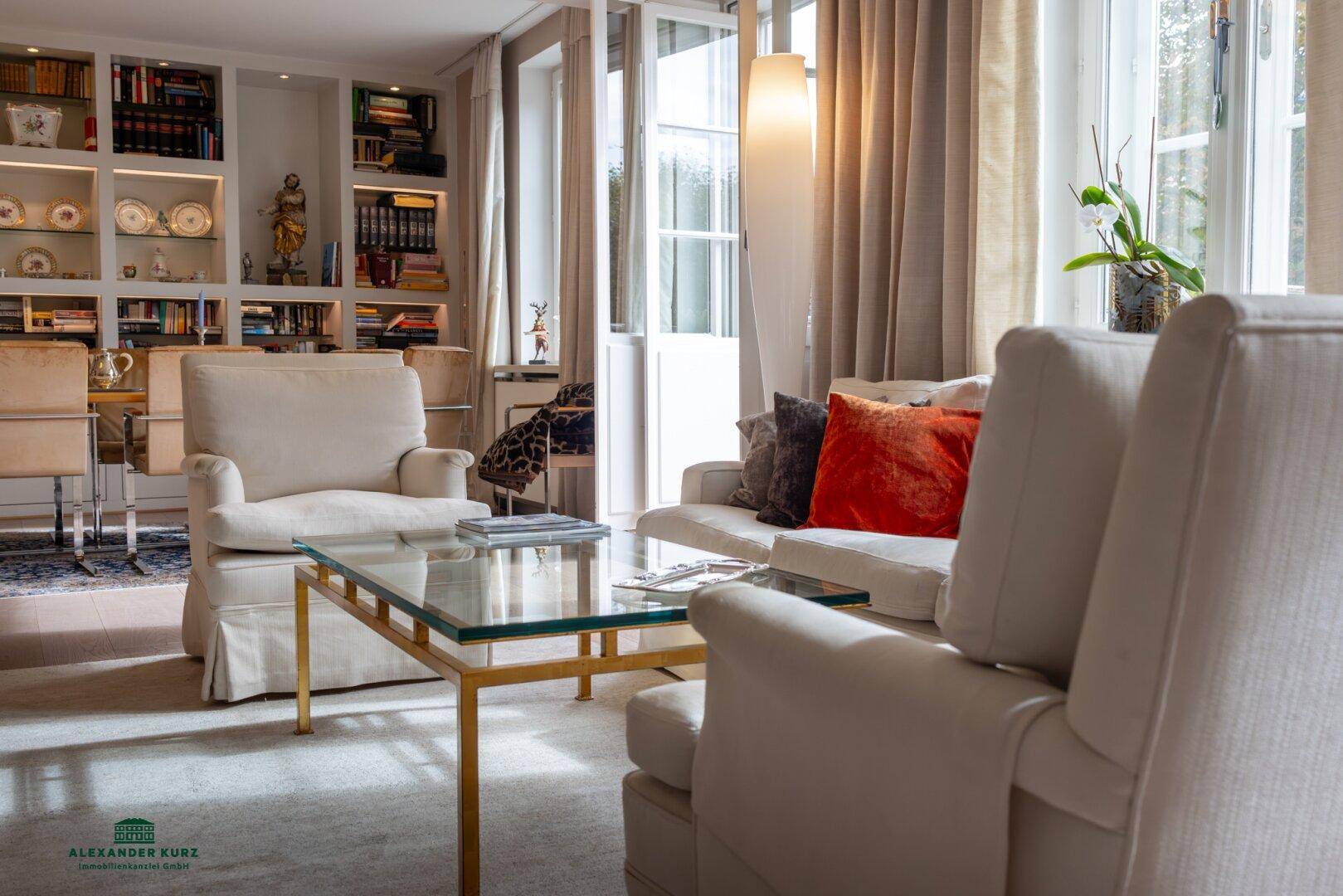 Gemütlicher Wohnbereich mit beigen Sofas, einem Glastisch und einem Essbereich mit Bücherregalen.