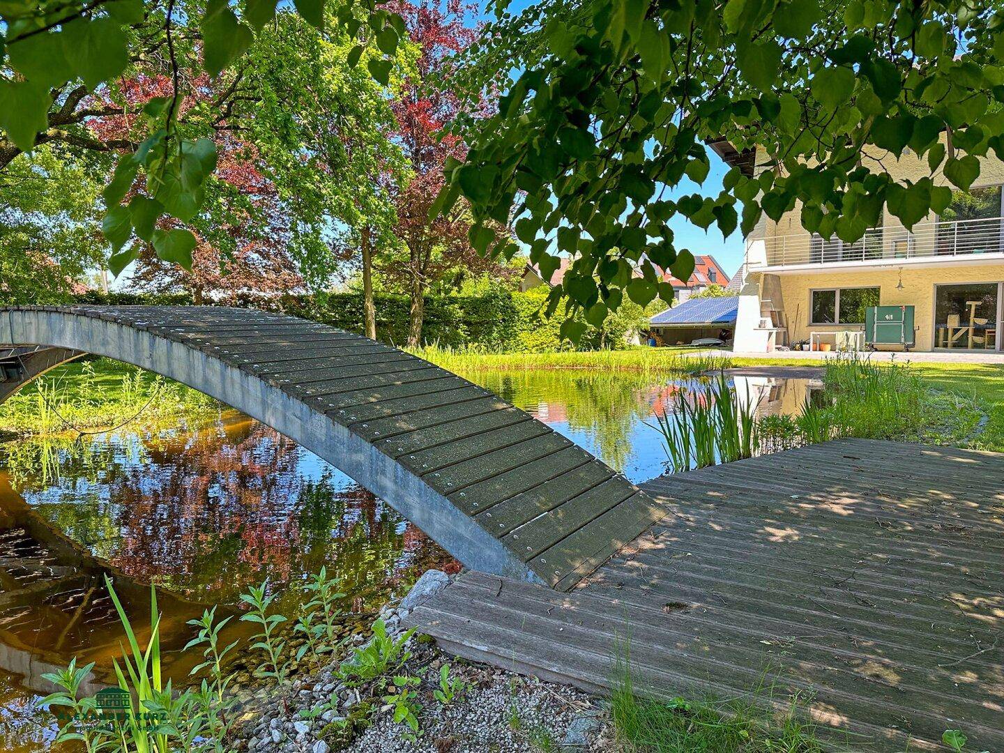 Idyllische Brücke über den Teich im weitläufigen Garten mit Blick auf das Haus.