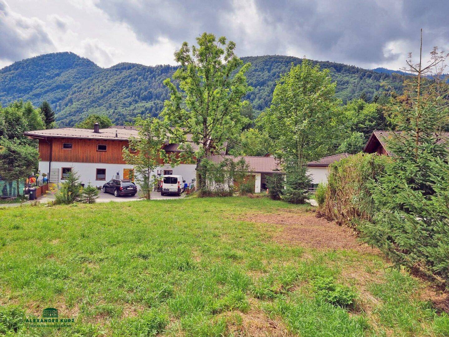 Haus mit großem Rasenbereich, umgeben von Bäumen und einer beeindruckenden Bergkulisse im Hintergrund.