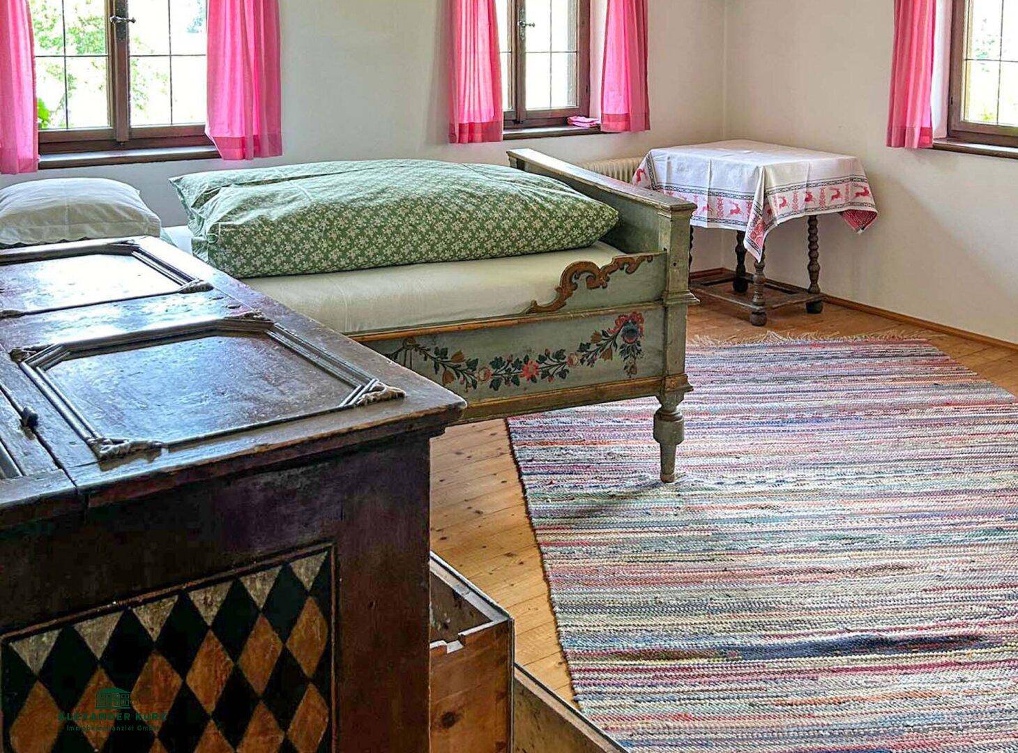 Gemütliches Schlafzimmer mit traditionellem, bemaltem Bett, Holzboden und farbenfrohem Teppich.