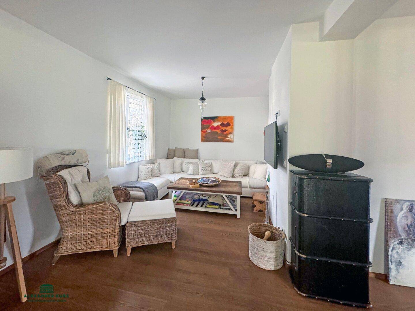 Gemütliches Wohnzimmer mit großem Ecksofa, Korbsessel und Holzboden, ideal zum Entspannen.