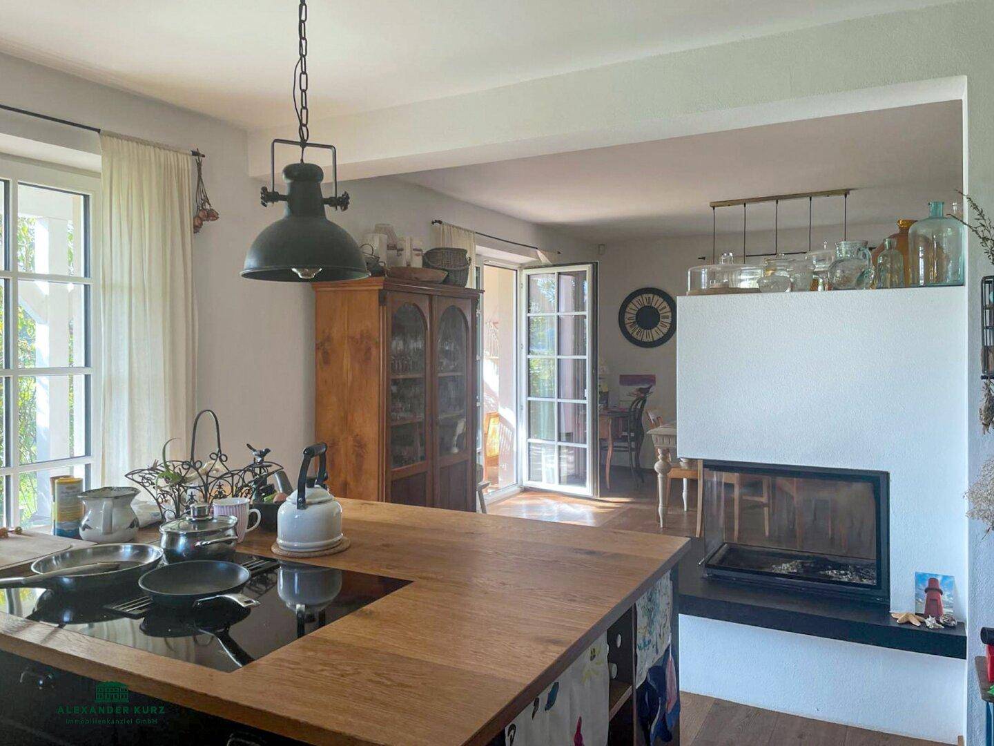 Moderne Küche mit Holz-Arbeitsplatte und Induktionskochfeld, offen zum Essbereich mit Kamin und Zugang nach draußen.