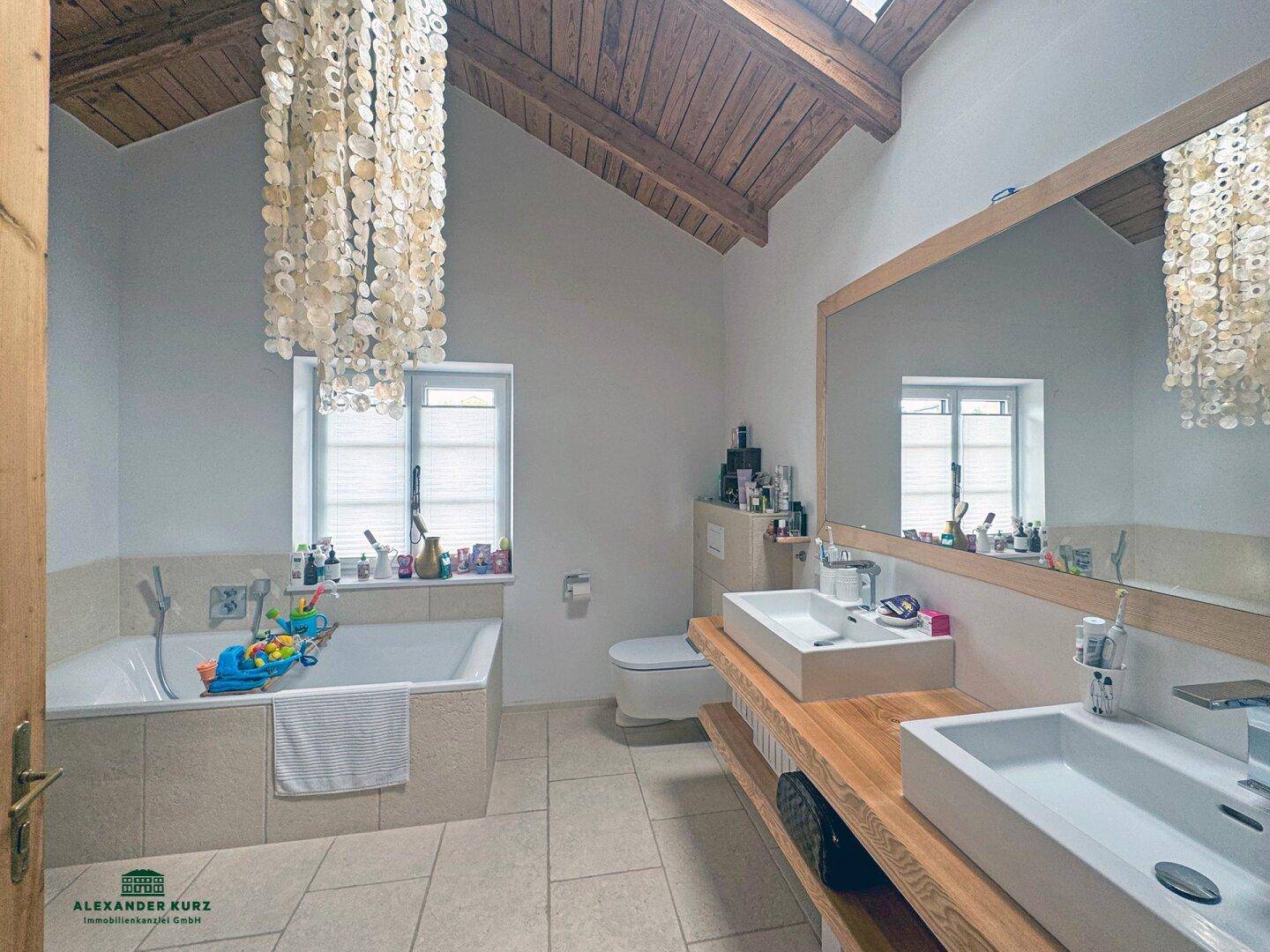 Geräumiges Badezimmer mit Doppelwaschbecken, Badewanne und Holzbalkendecke, beleuchtet durch ein Dachfenster.