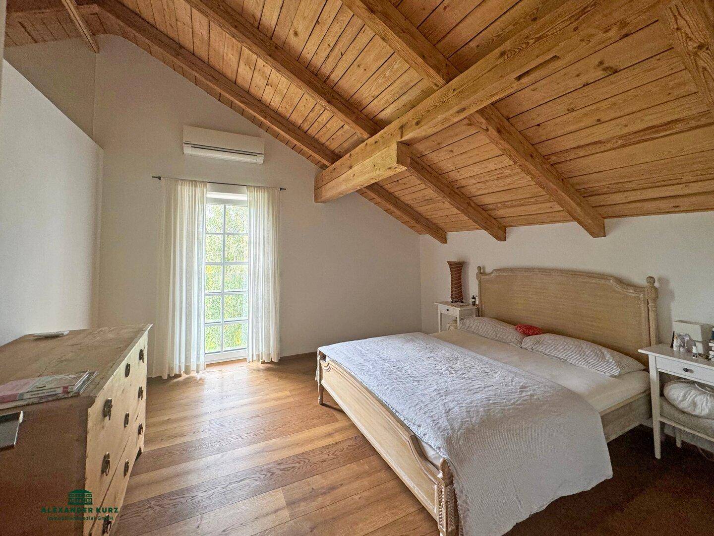 Helles Schlafzimmer mit Holzbalkendecke, Holzboden und Zugang zum Außenbereich, ausgestattet mit Klimaanlage.