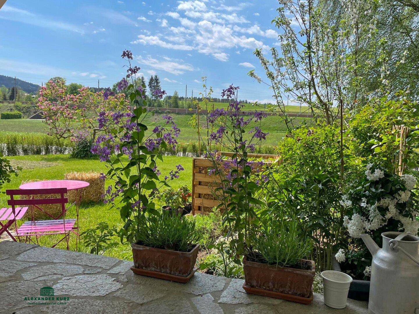 Idyllischer Gartenbereich mit bunten Blumen und Sitzgelegenheiten, bietet einen weiten Blick auf die grüne Landschaft.