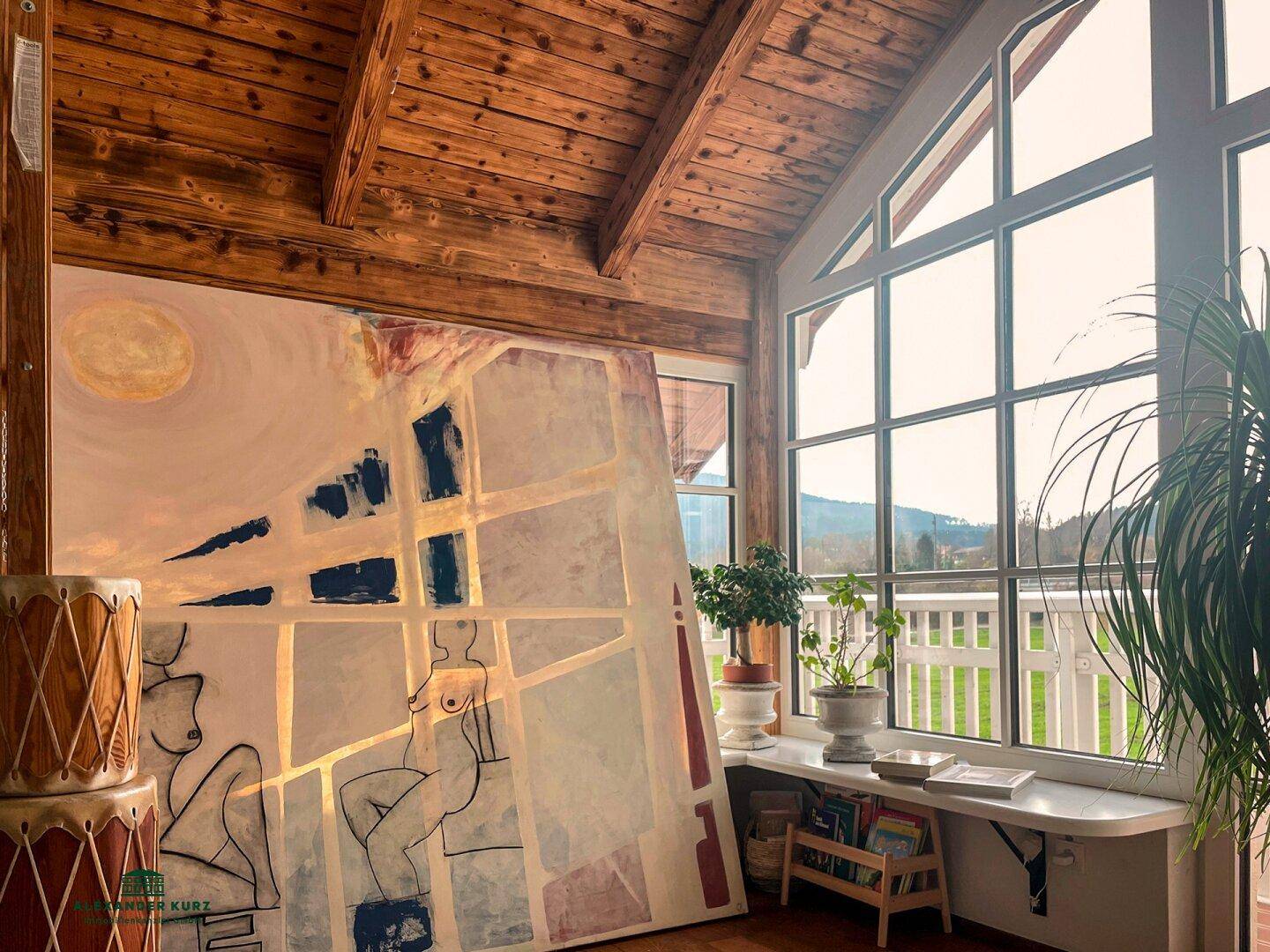 Heller Raum mit großen Fenstern, Holzbalkendecke und Kunstwerk, bietet einen schönen Ausblick ins Grüne.
