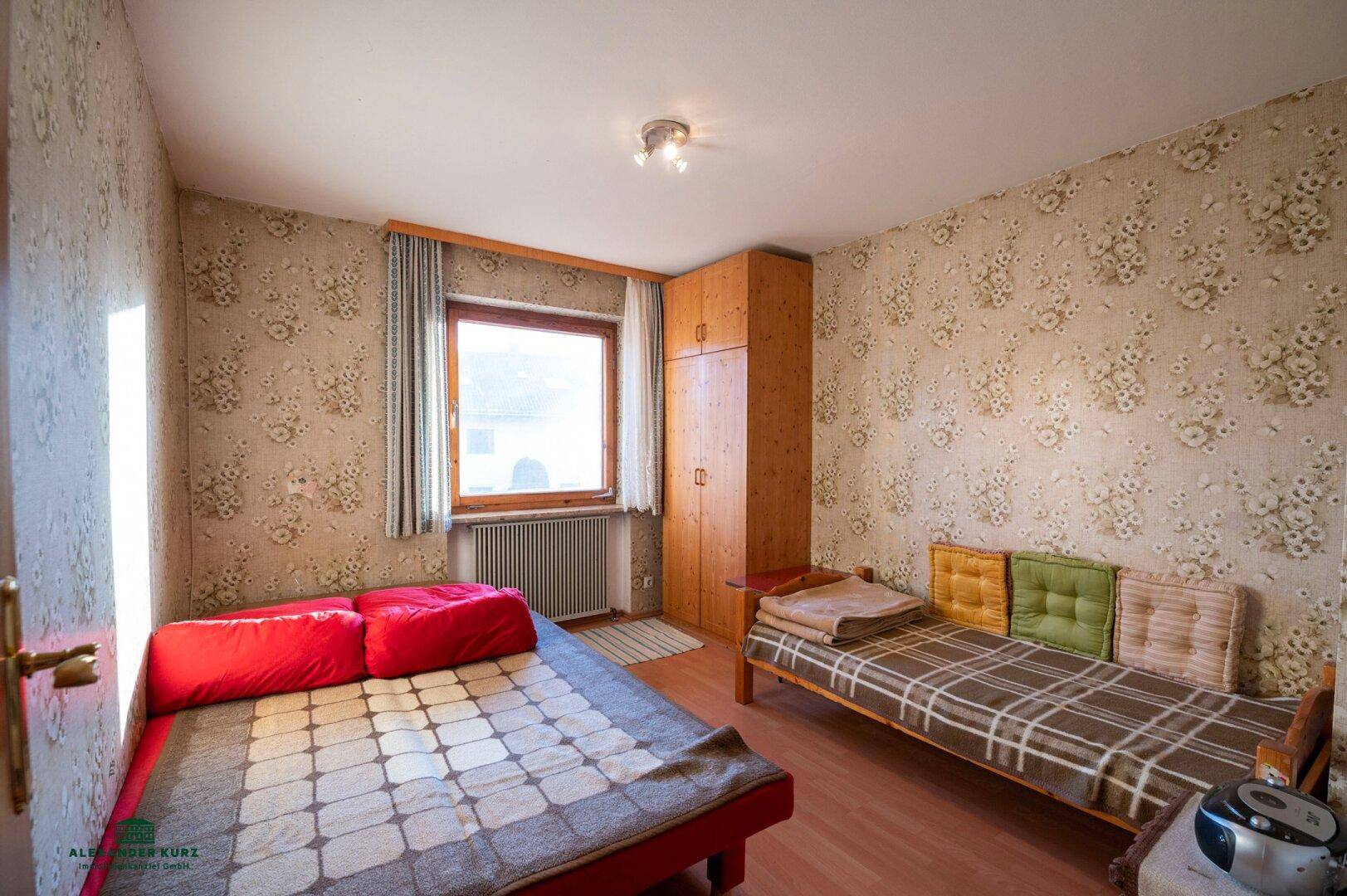 Gemütliches Schlafzimmer mit floraler Tapete, Holzmöbeln und zwei Einzelbetten.