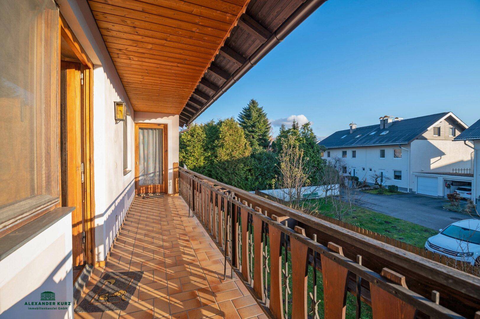 Sonniger Balkon mit Fliesenboden, Holzgeländer und Blick auf die Nachbarschaft.