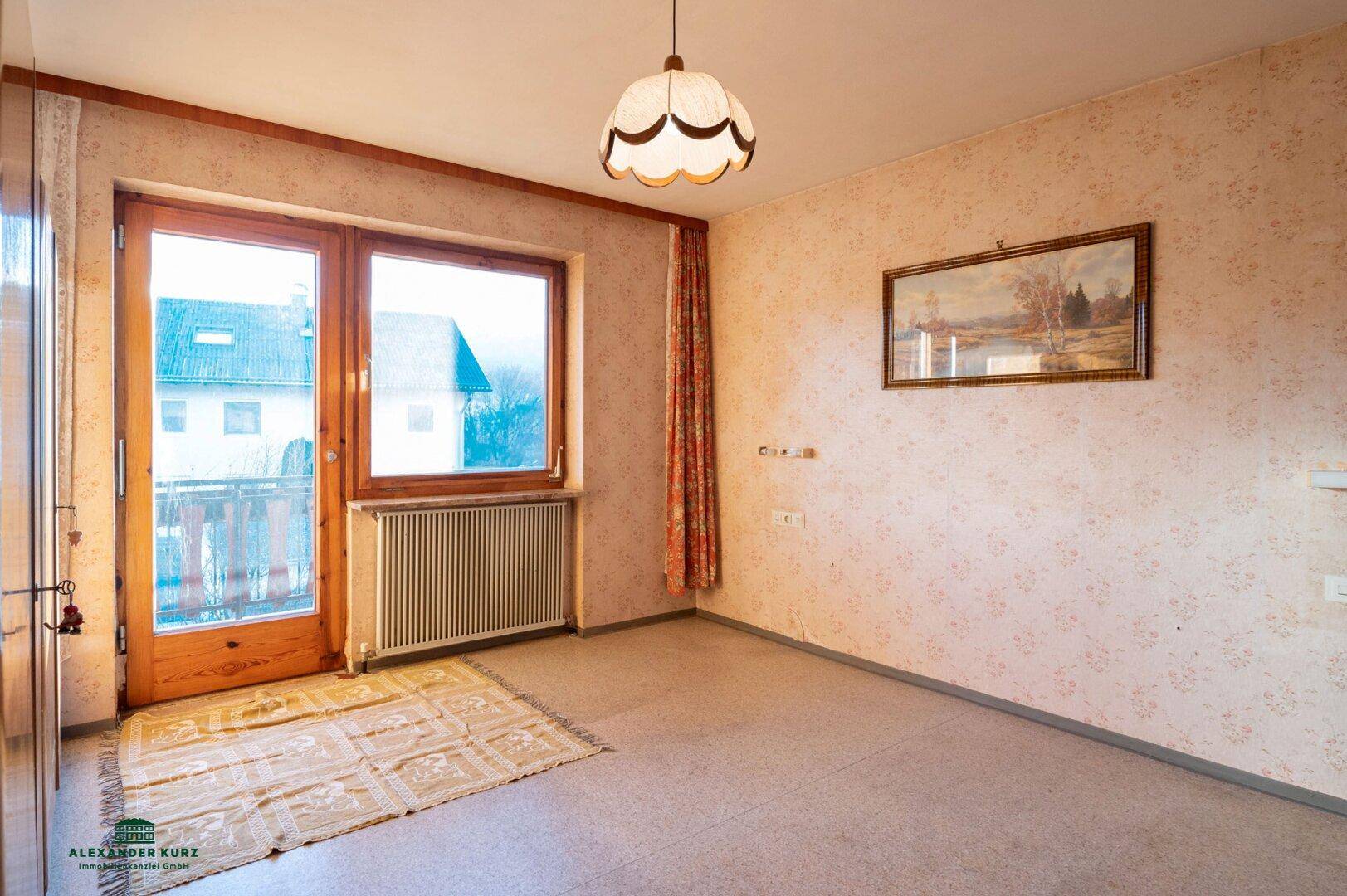 Heller Raum mit floraler Tapete, Teppichboden und direktem Zugang zum Balkon.