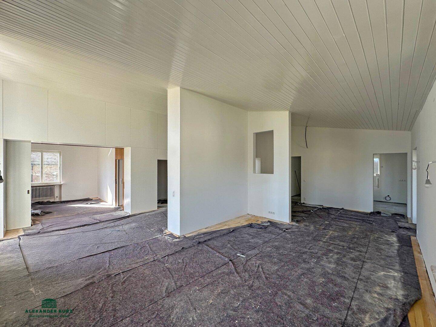 Großer Innenraum im Rohbau mit Schutzfolie auf dem Boden und Holzdeckenpaneelen, bereit für den Ausbau.