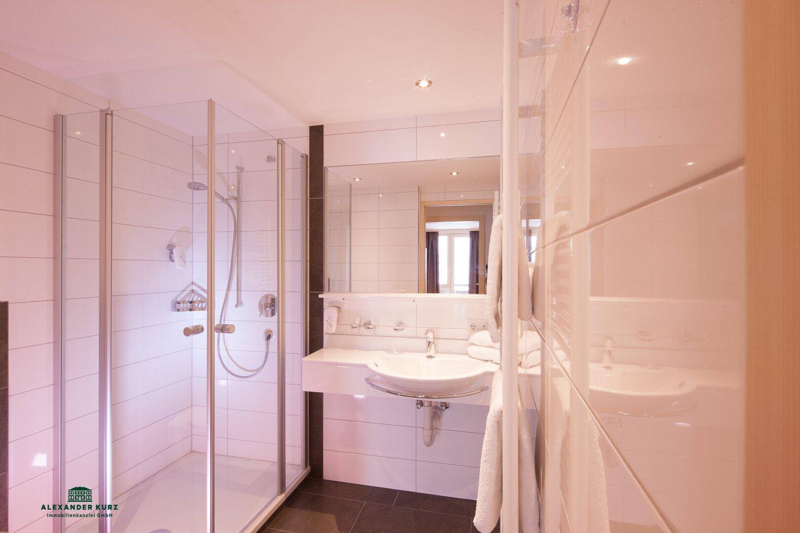Modernes Badezimmer mit weiß gefliesten Wänden, ebenerdiger Dusche und einem Waschbecken.