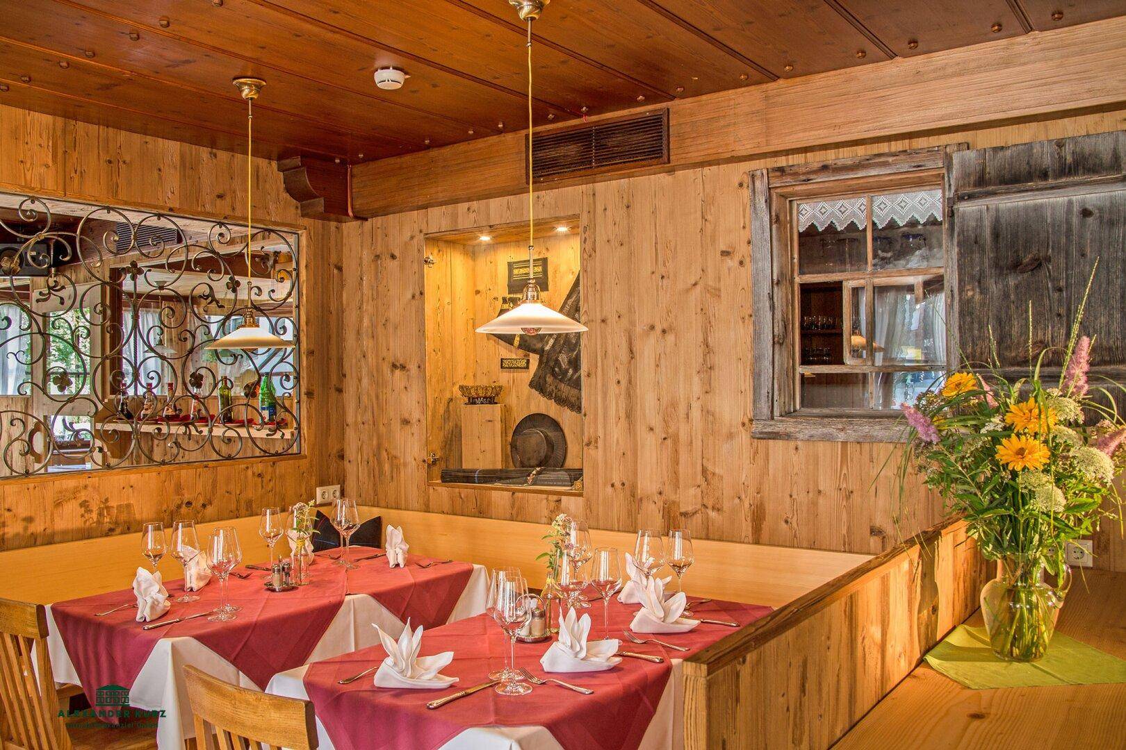 Gemütlicher Essbereich im traditionellen Stil mit Holztäfelung, roten Tischdecken und Blumen.