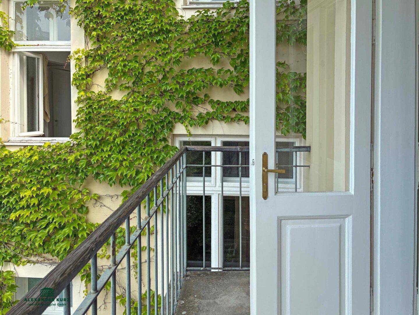 Balkon mit Blick auf eine von Efeu bewachsene Gebäudefassade und offener Balkontür.