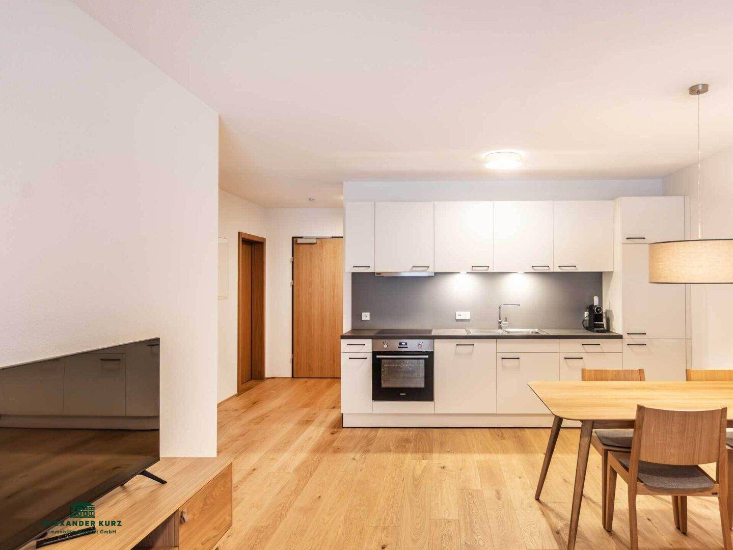 Moderne Einbauküche mit weißen Schränken und integriertem Essbereich in hellem Ambiente.