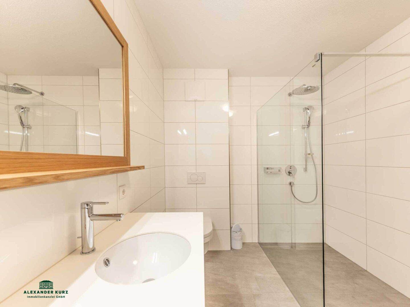 Modernes Badezimmer mit großer begehbarer Dusche, weiß gefliesten Wänden und Einzelwaschbecken.