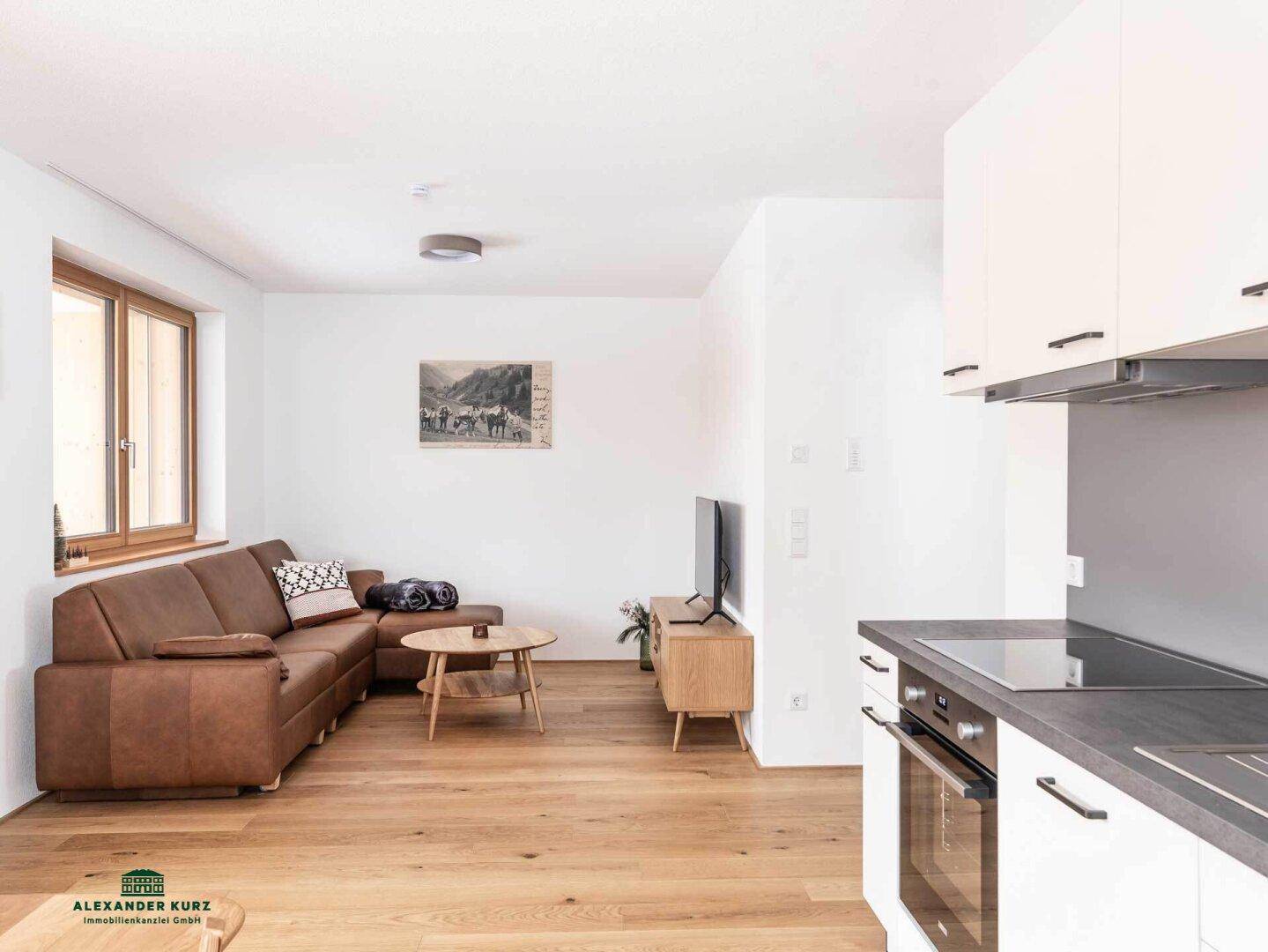 Heller Wohnbereich mit bequemer Couch, Holzboden und offenem Übergang zur Küche.