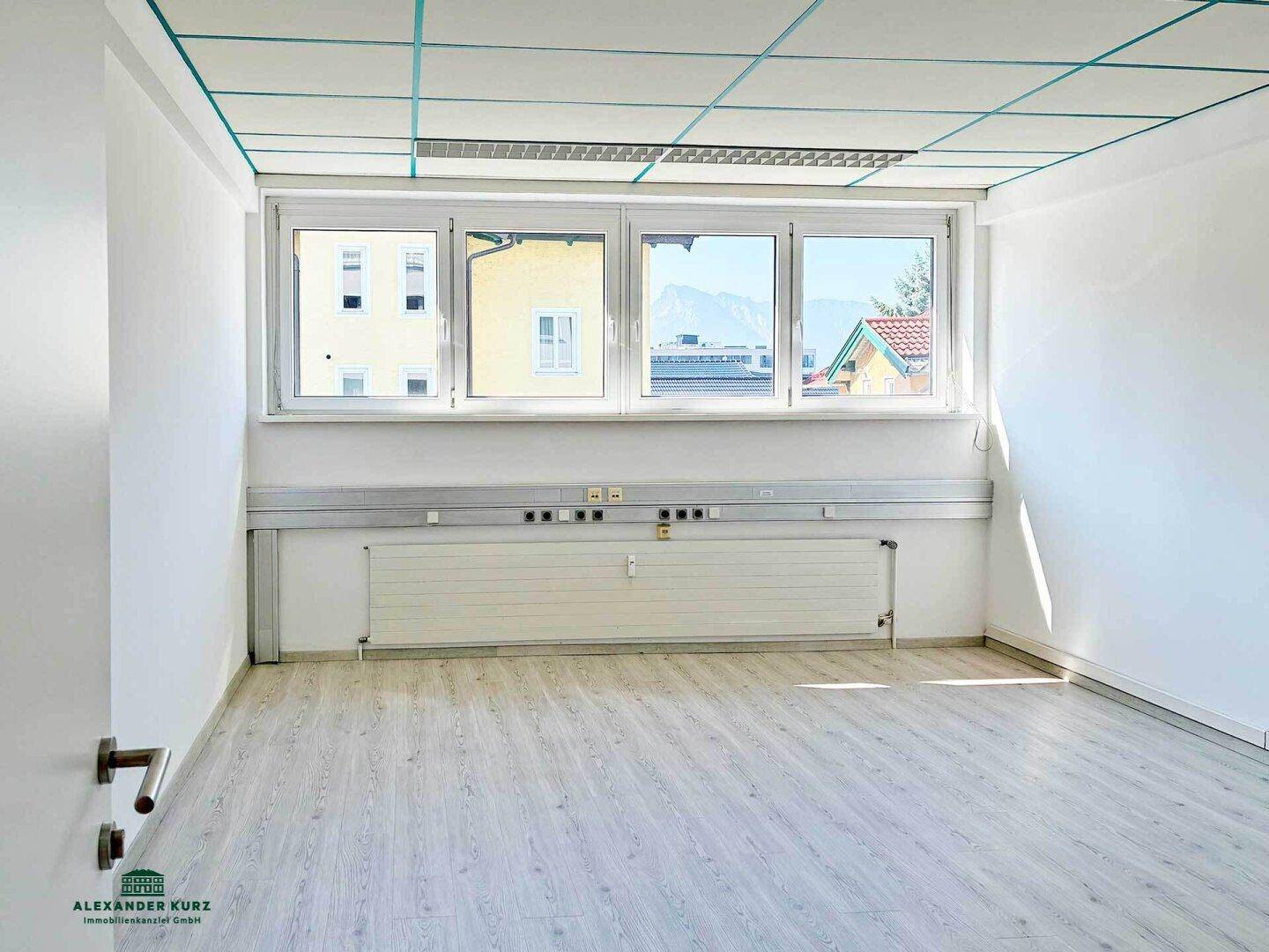 Heller Büroraum mit großen Fenstern, Laminatboden und Blick auf Berge und Umgebung.