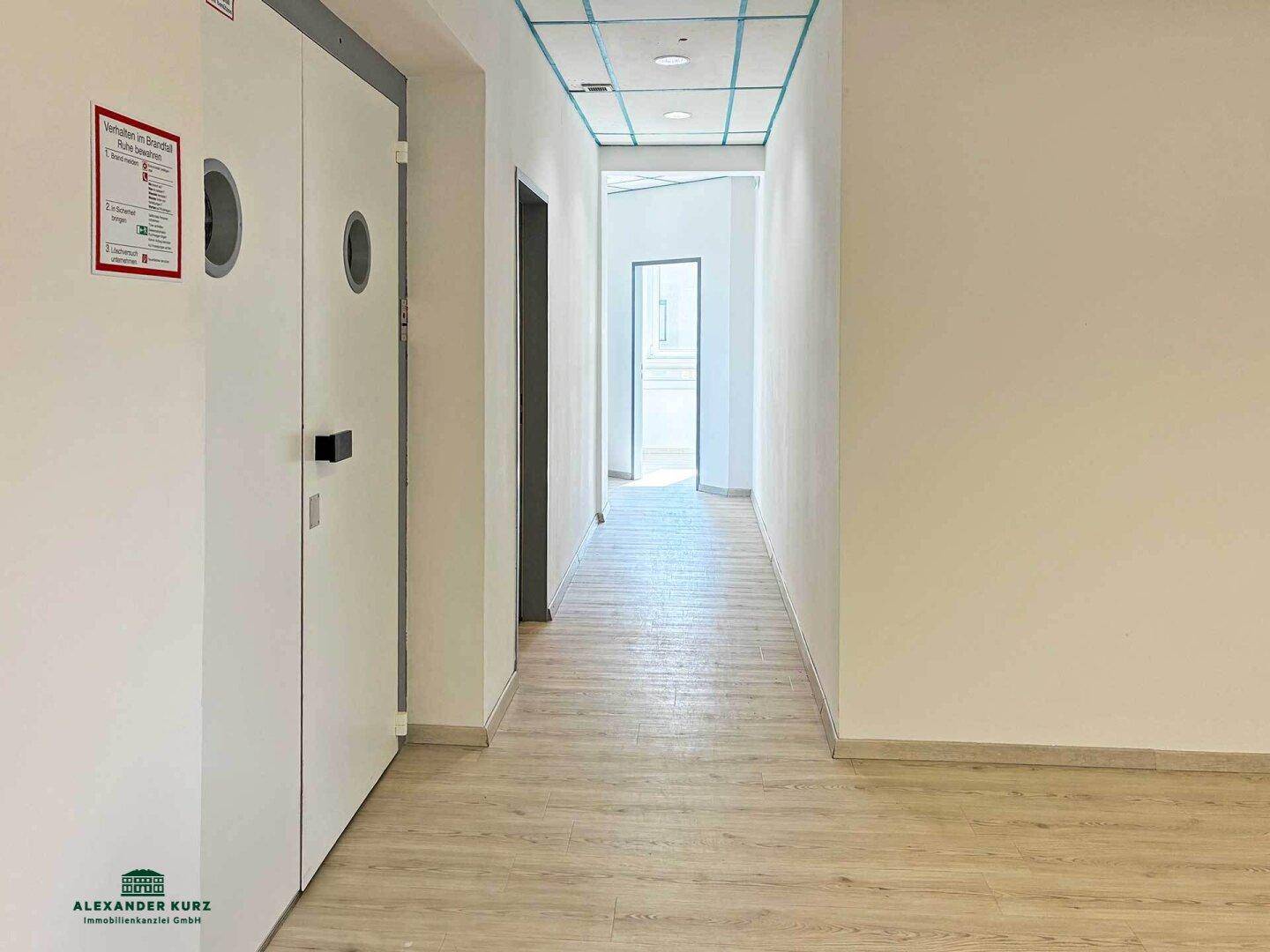 Langer Flur mit Laminatboden, weißen Wänden und Türen, die zu weiteren Räumen führen.