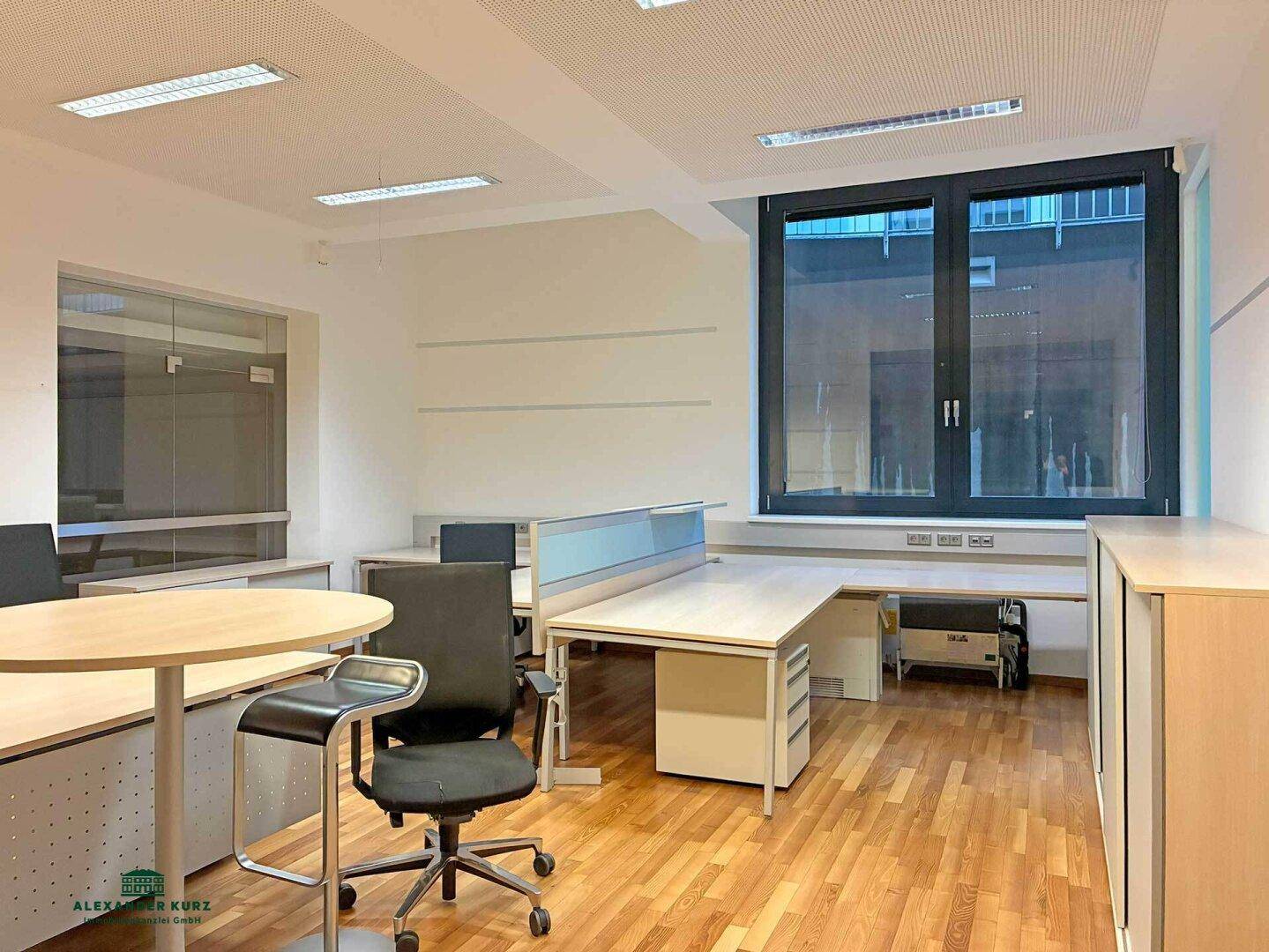 Offener Bürobereich mit mehreren Arbeitsplätzen, modernen Büromöbeln und großen Fenstern für viel Tageslicht.