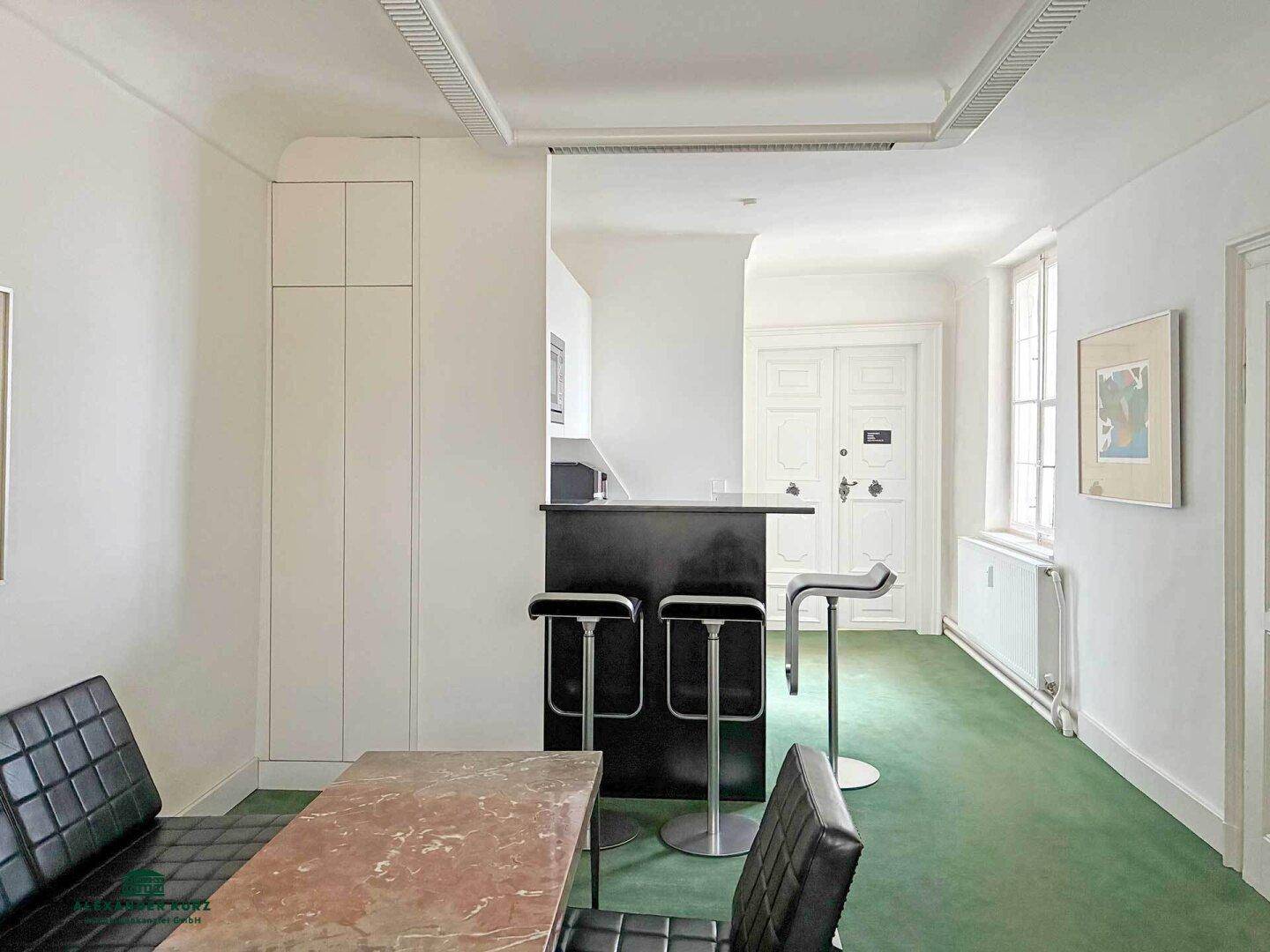Kompakte Küchenzeile mit Bar und Essbereich, ergänzt durch einen grünen Teppichboden und Einbauschränke.