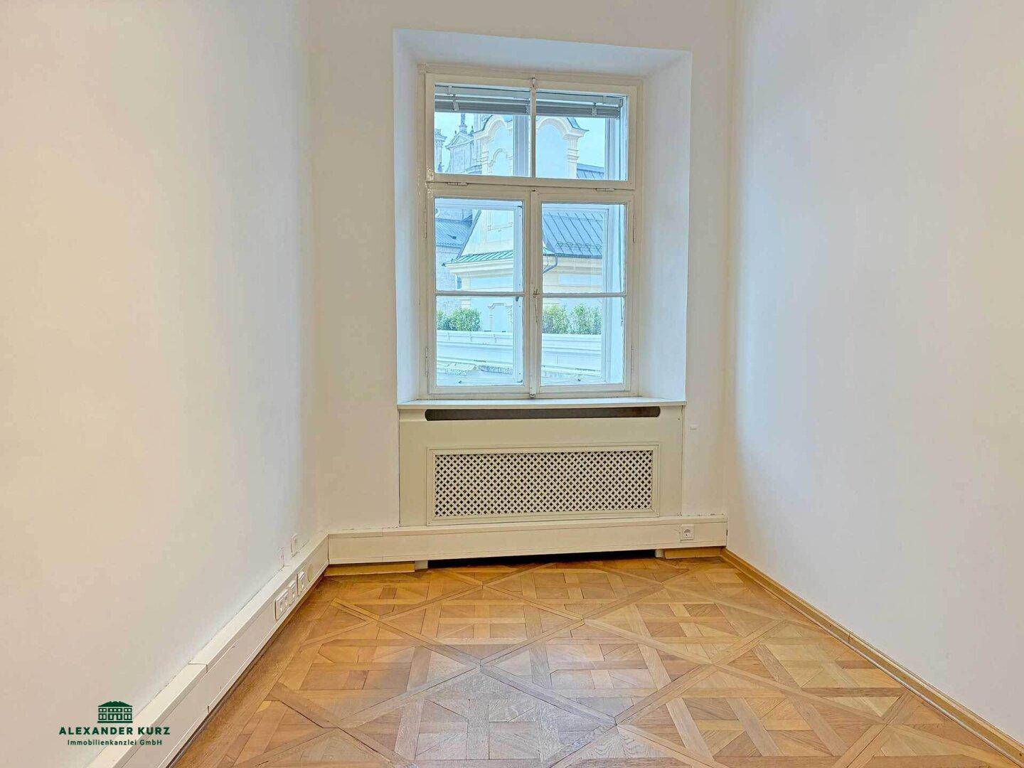 Kleiner, heller Raum mit einem Fenster und klassischem Fischgrätparkettboden, ideal als Arbeitszimmer.