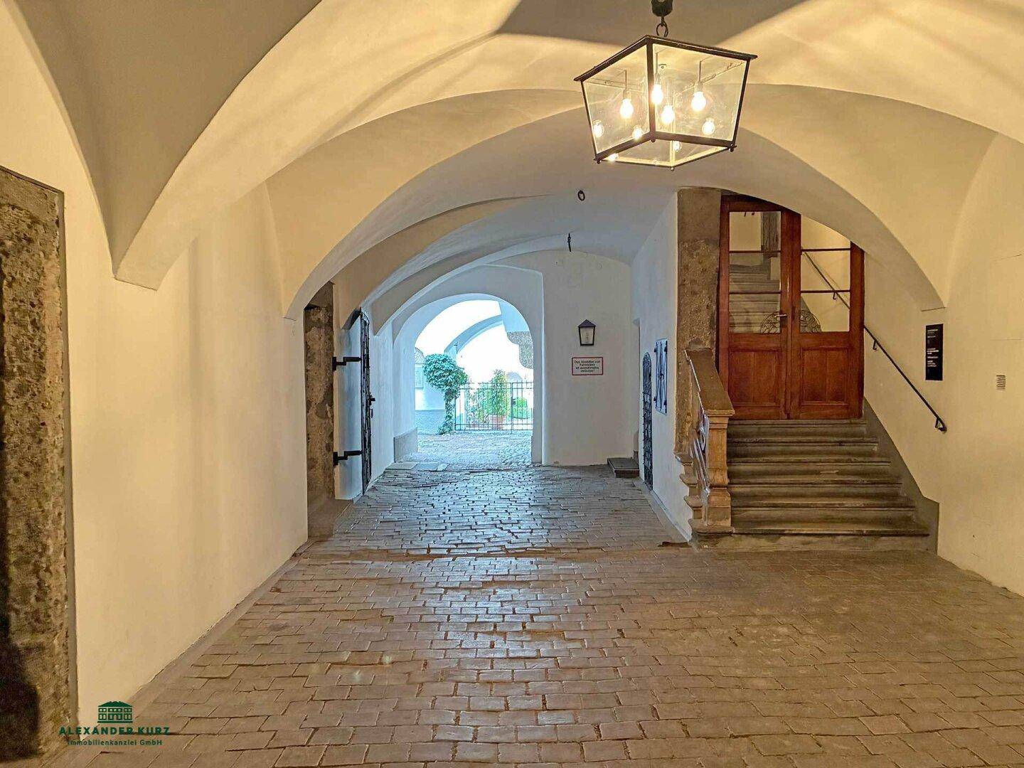 Historischer Durchgang mit Gewölbedecke, Kopfsteinpflaster und Blick auf einen charmanten Innenhof.