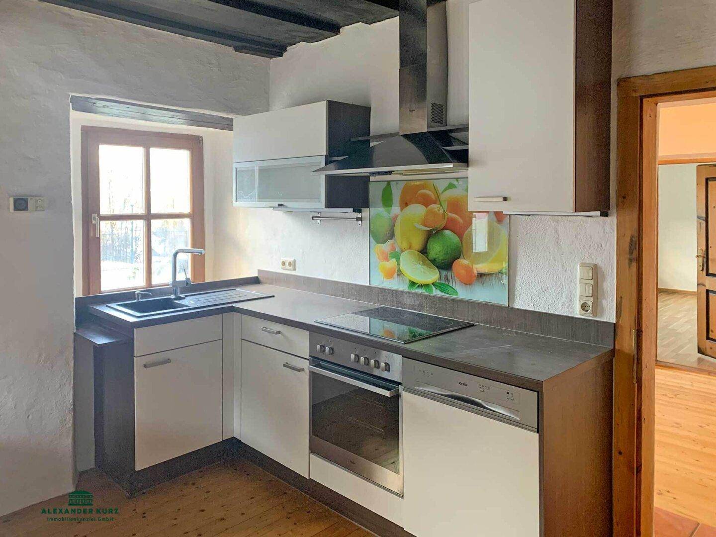 Helle Küche mit modernen weißen Schränken, Induktionskochfeld und Fensterblick ins Grüne.