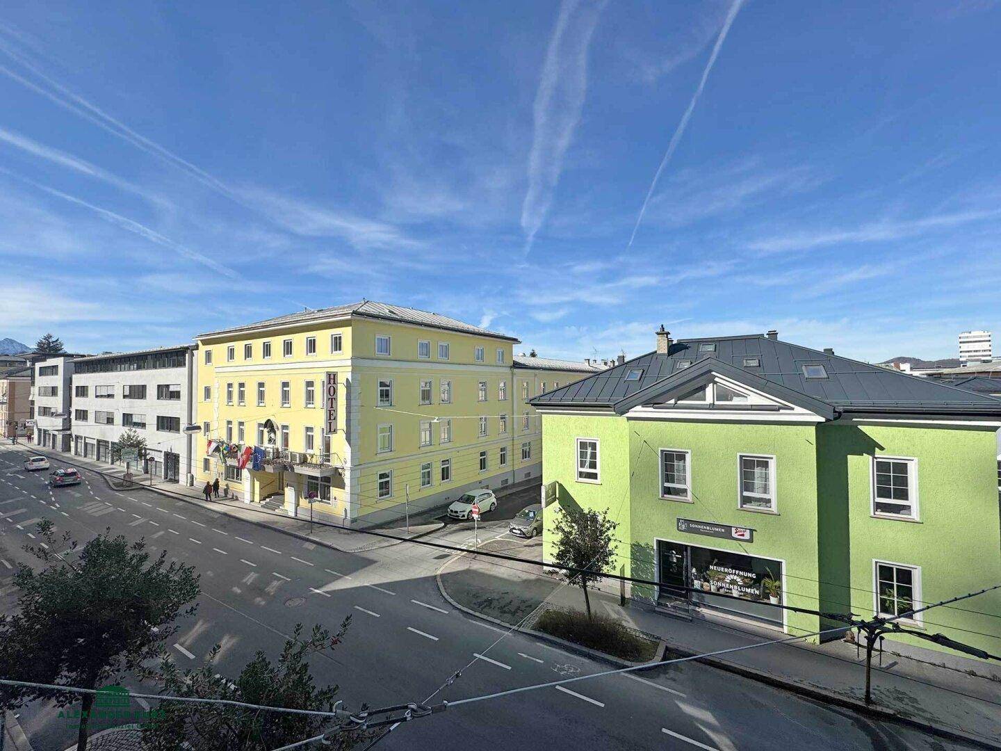 Blick auf eine belebte Straße mit verschiedenen Gebäuden unter blauem Himmel und Sonnenschein.