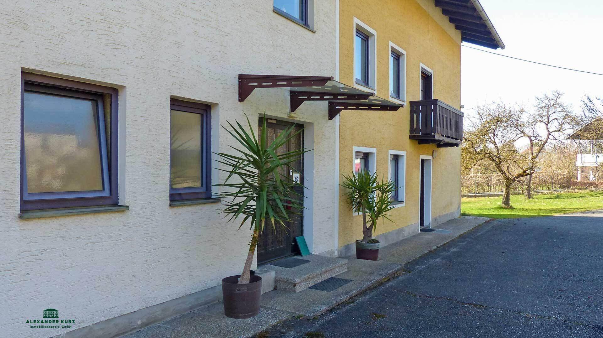 Eingangsbereich des Hauses mit Vordach und Topfpflanzen, daneben ein kleiner Balkon.